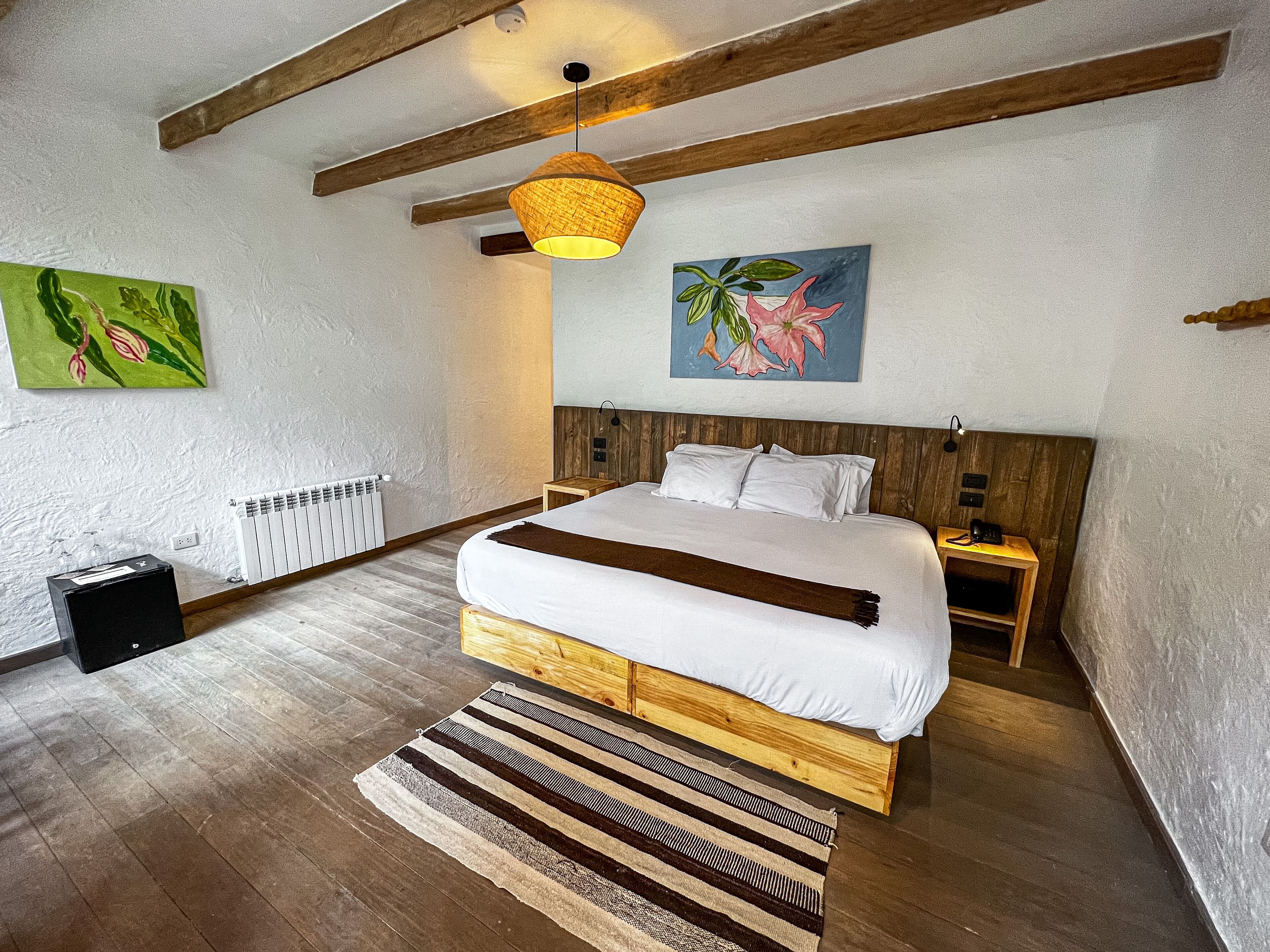 Un dormitorio con una cama de madera, una lámpara colgante, un radiador y un cuadro en la pared.