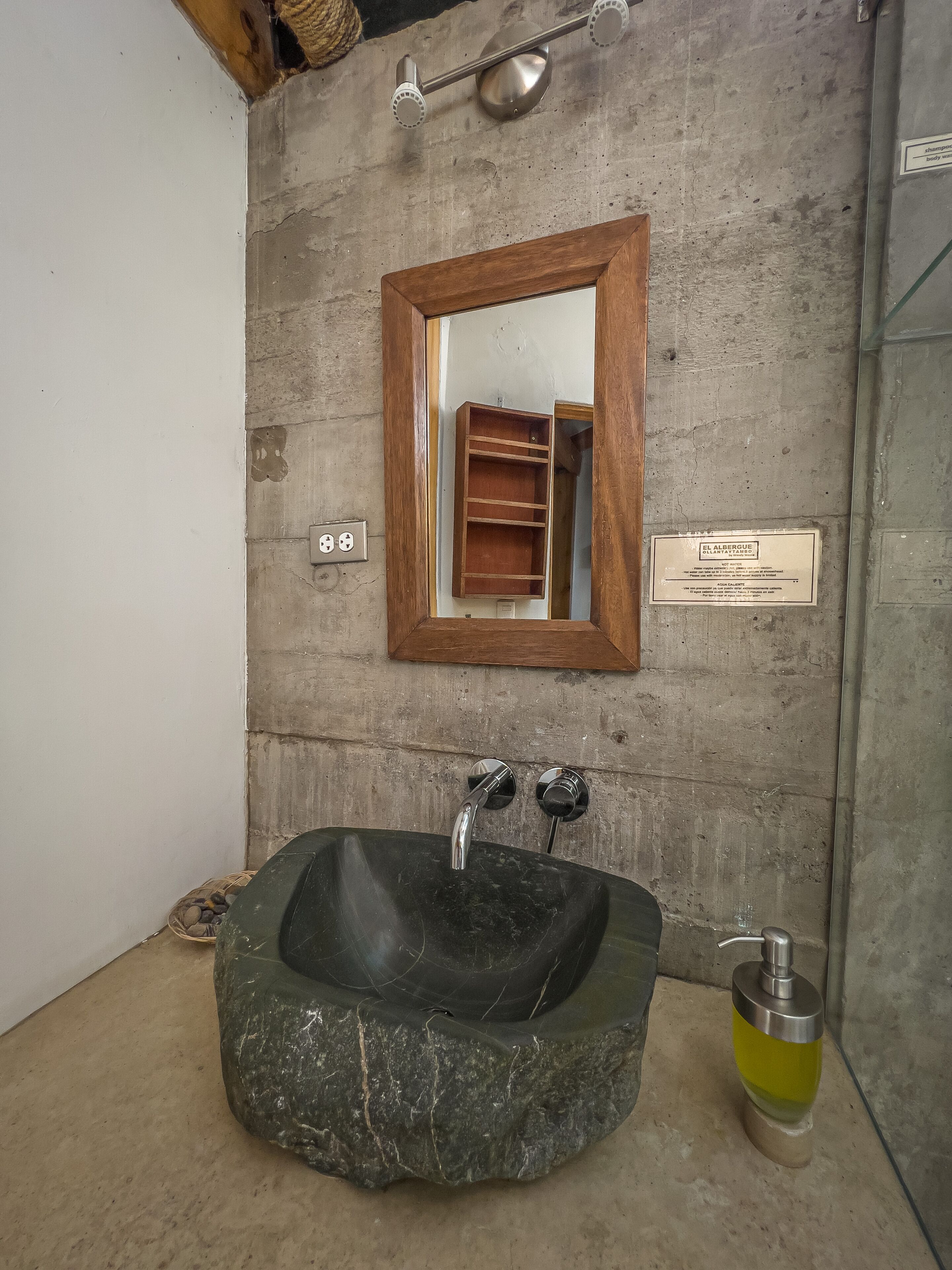 A bathroom with a stone sink, a wooden-framed mirror, and a showerhead.