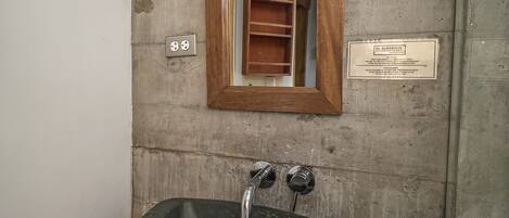 A bathroom with a stone sink, a wooden-framed mirror, and a showerhead.