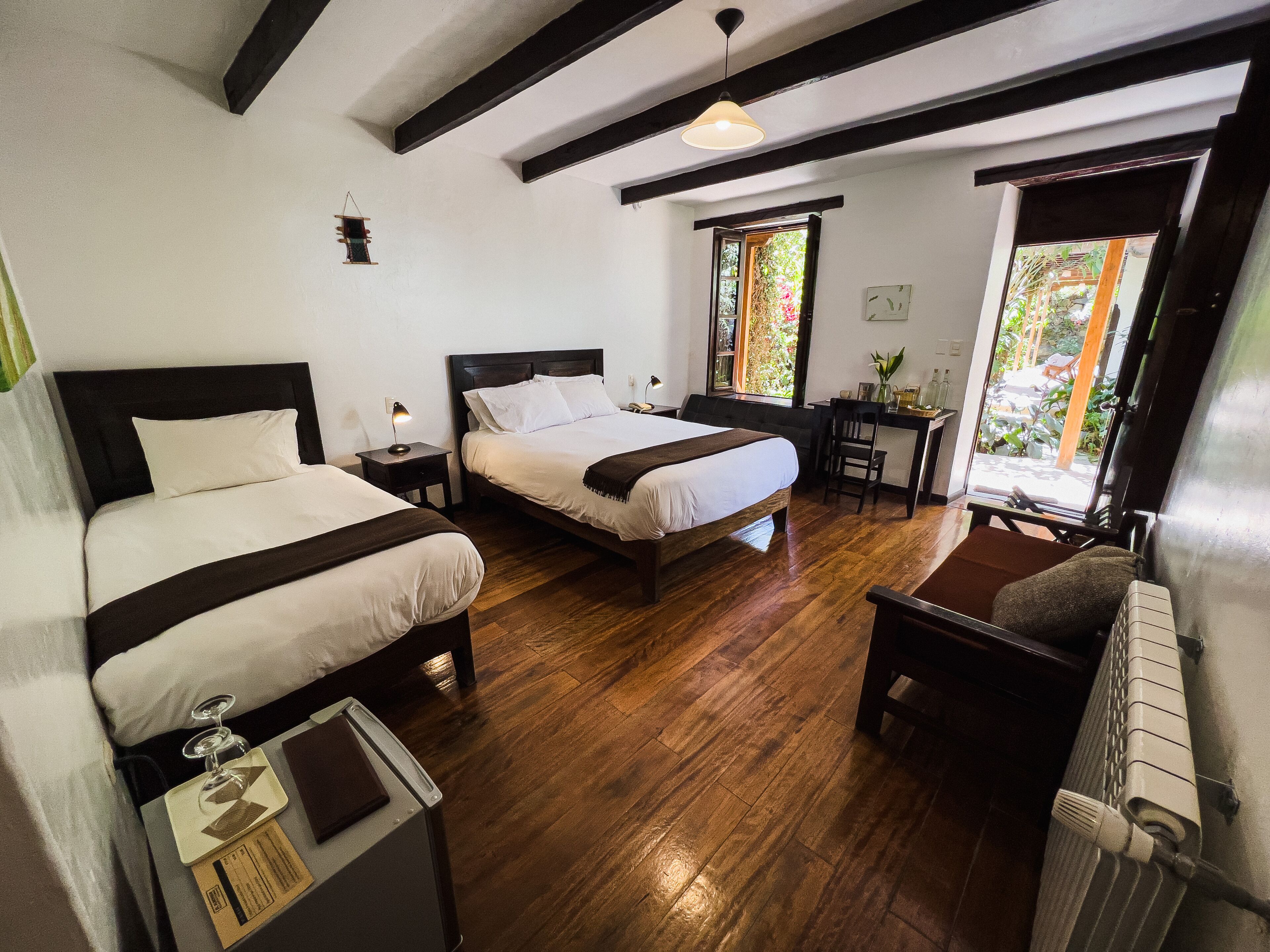 Camera d'albergo con due letti, una scrivania e una sedia. Una finestra offre vista sul verde circostante.
