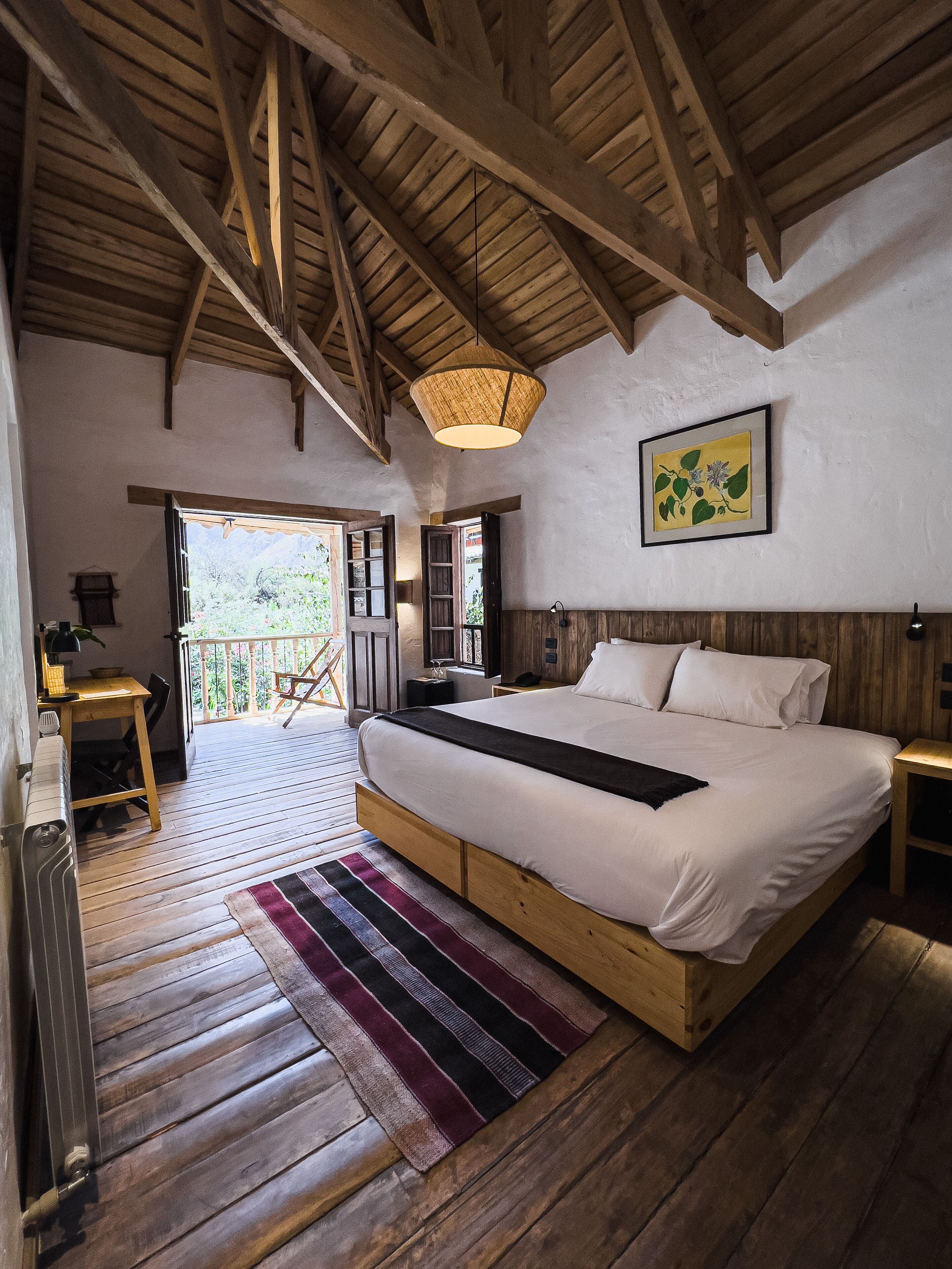 Un dormitorio espacioso con una cama grande, vigas de madera, una lámpara colgante y vistas al exterior.