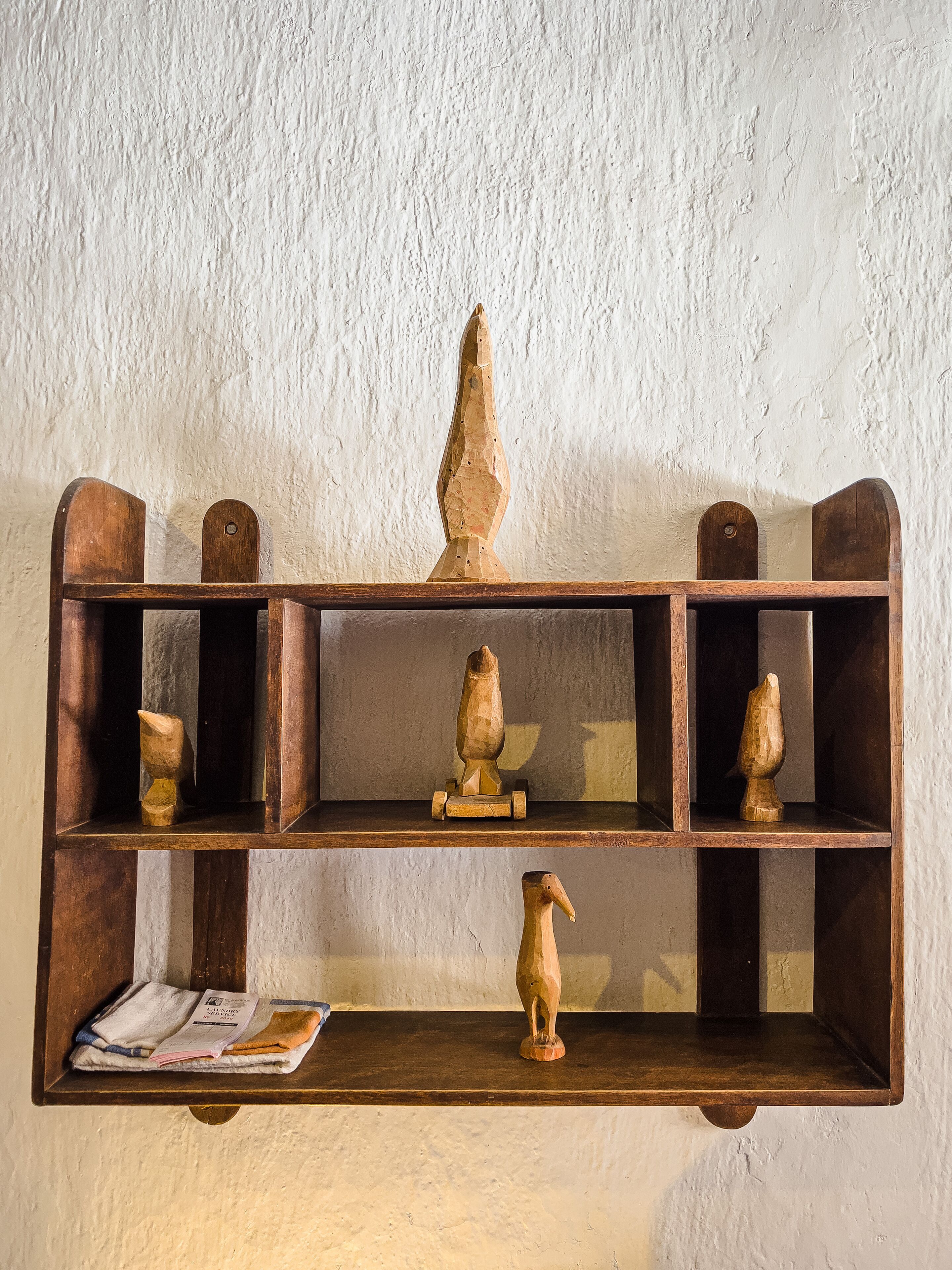 Una estantería de madera con tres esculturas de madera y un periódico doblado.