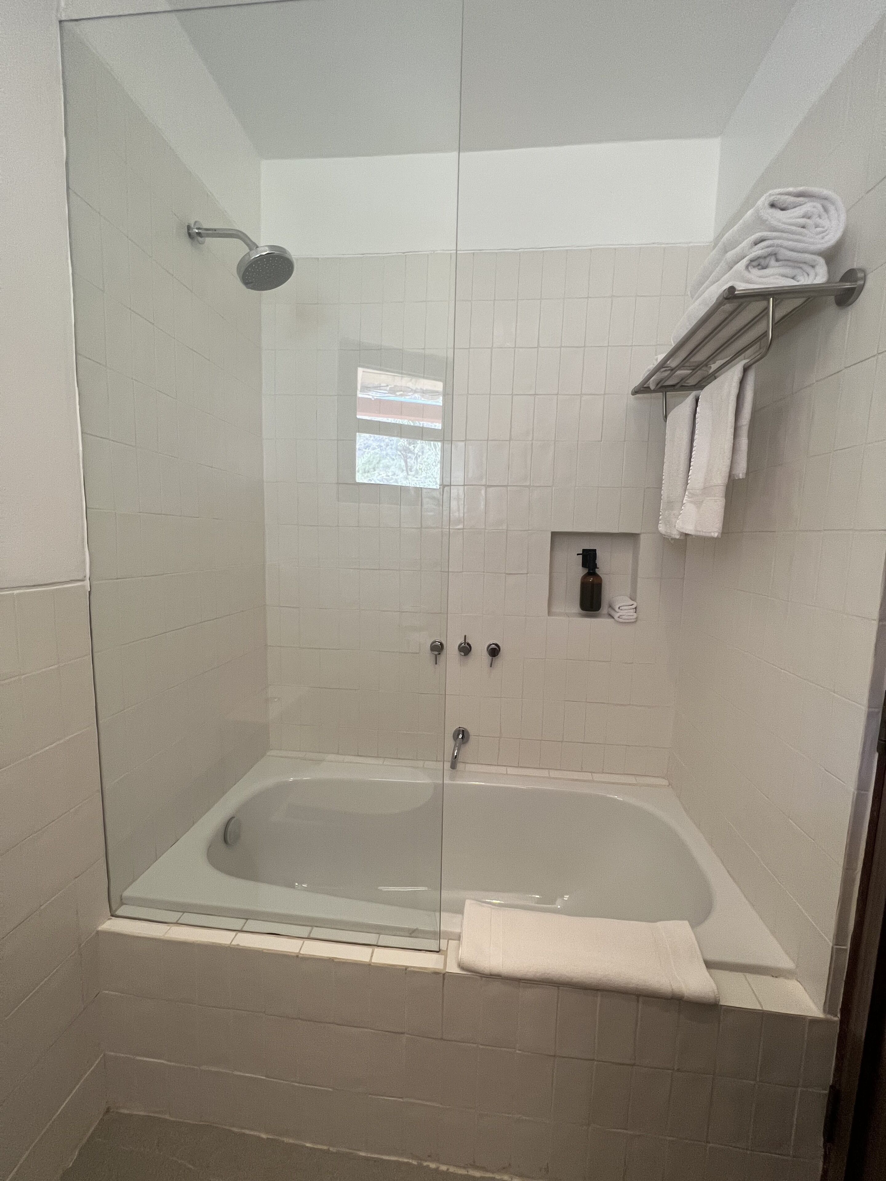 A walk-in shower with a glass door, a bathtub, and a towel rack with towels.