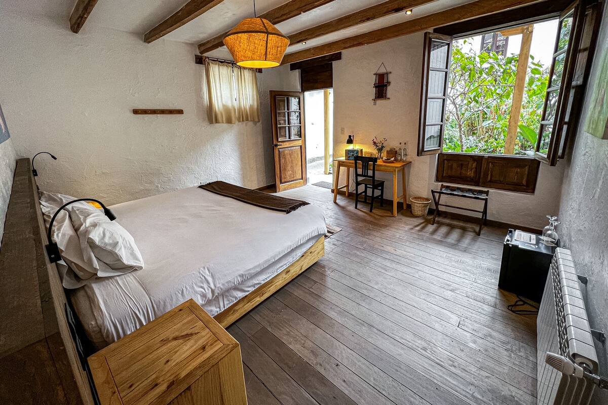 Een slaapkamer met een houten bed, een bureau en een raam met uitzicht op groen.