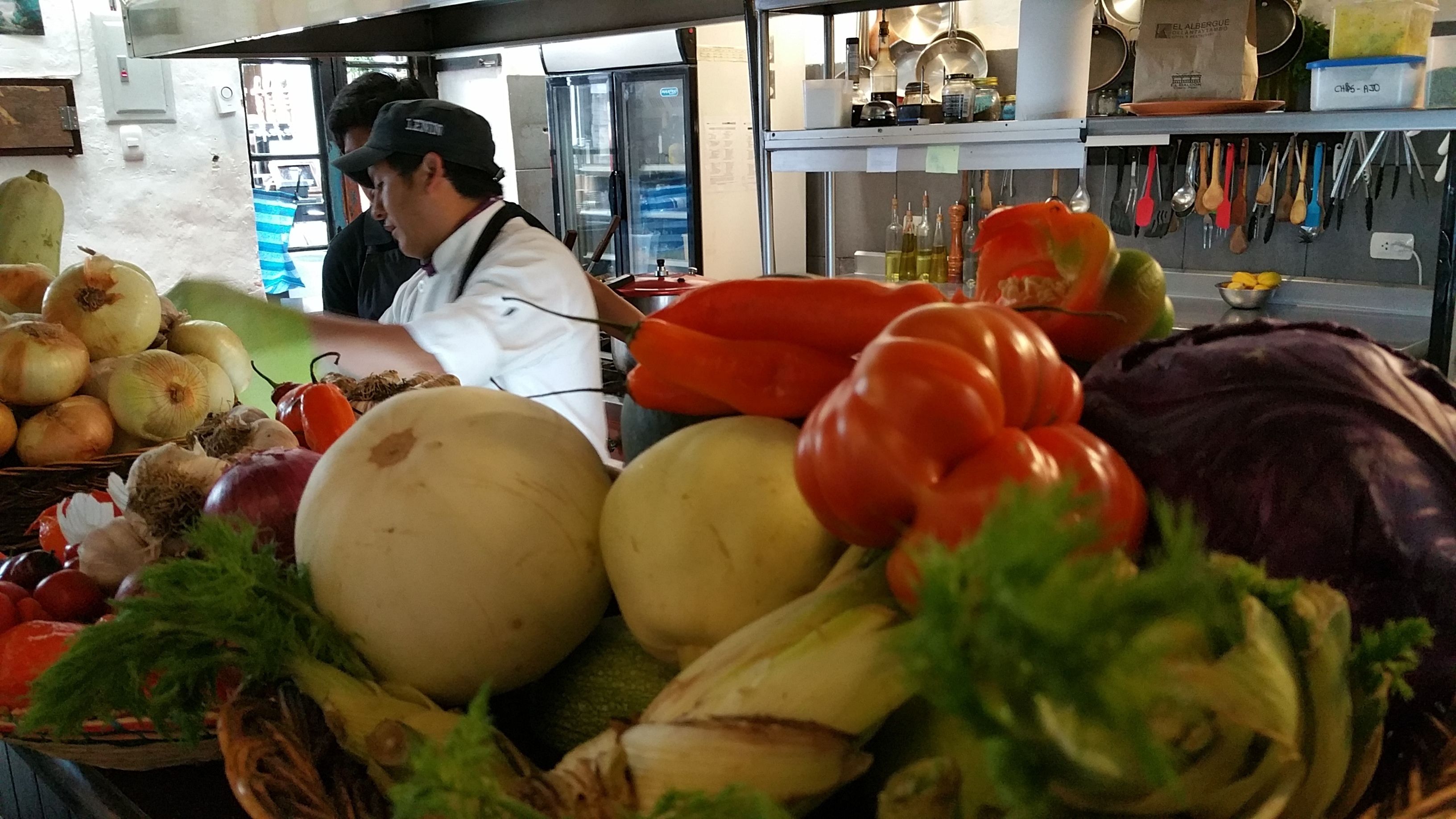 Un puesto de mercado con productos frescos, incluyendo cebollas, tomates y verduras de hoja.