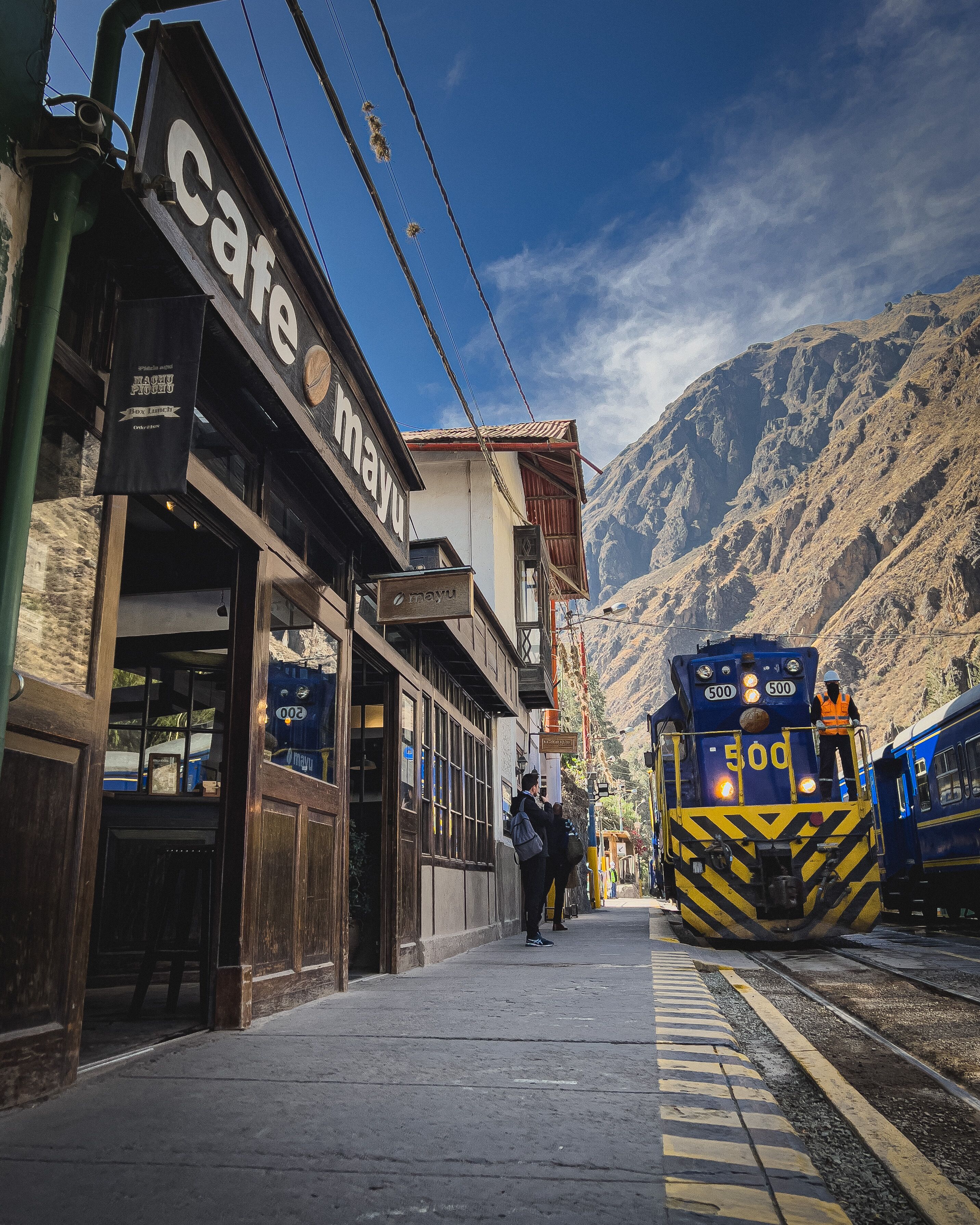 Un café avec une vue sur les montagnes, un train portant le numéro 500 sur sa façade, et une personne debout sur le quai.