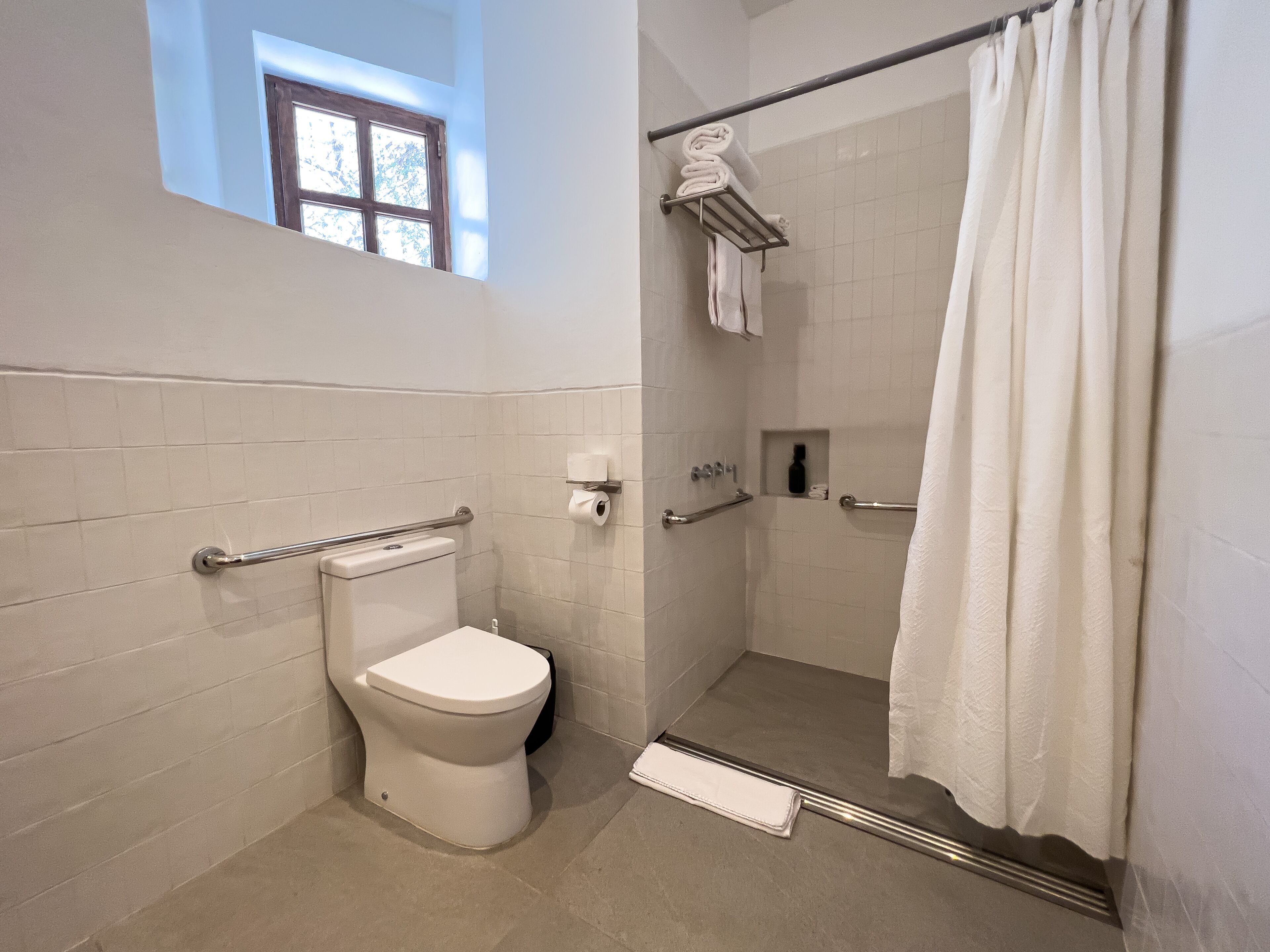 A bathroom with a toilet, shower, and a window.