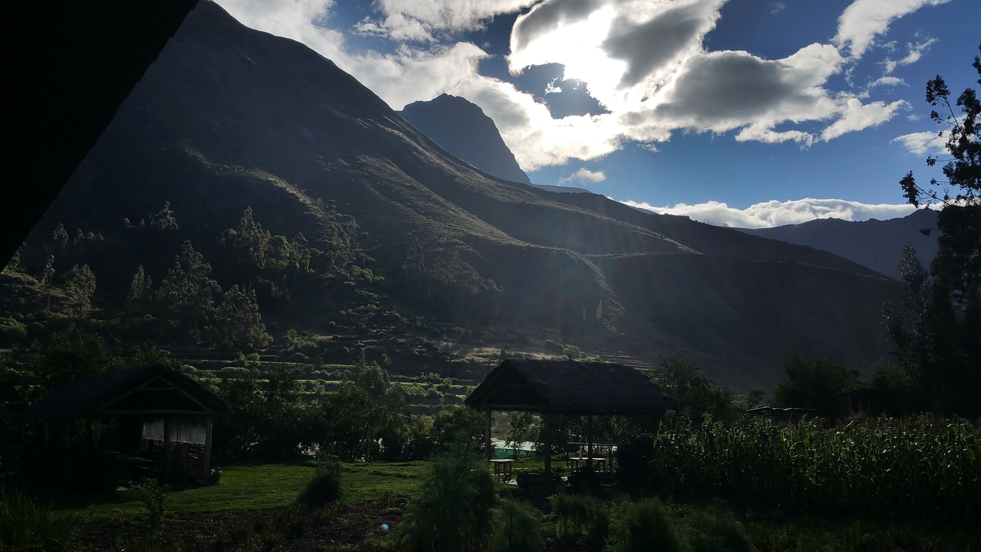 A mountainous landscape with a small house and a gazebo in the foreground.