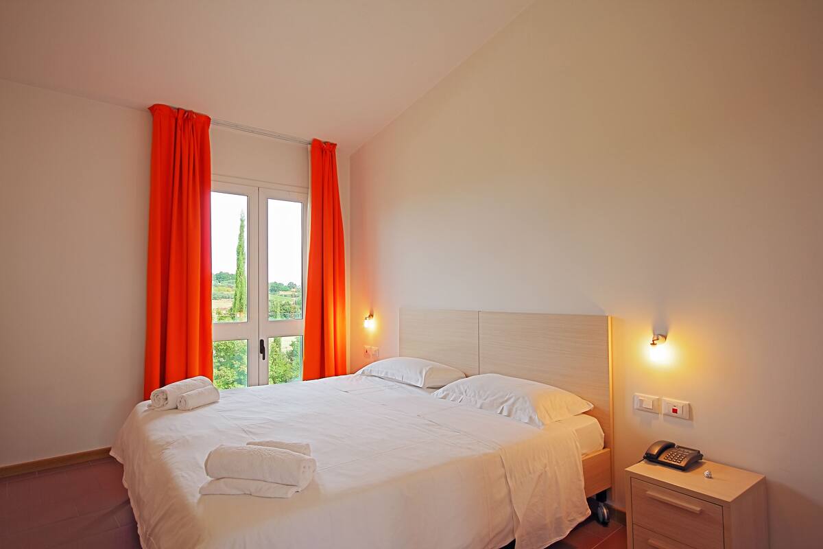 A hotel room with a large bed, two bedside tables, a nightstand with a phone, and a window with curtains.