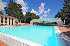Une piscine à l’eau d’un bleu cristallin, entourée de chaises longues et d’un espace abrité doté d’un toit en verre.