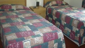 Ein Zimmer mit zwei hölzernen Betten, jedes mit einer gesteppten Tagesdecke. Dazwischen steht ein Nachttisch mit einer Lampe.