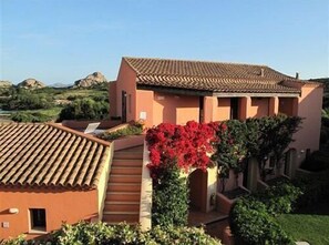 A two-story building with a tiled roof, a small staircase, and a red flowering bush. - Hotel Tre Monti (Arzachena)