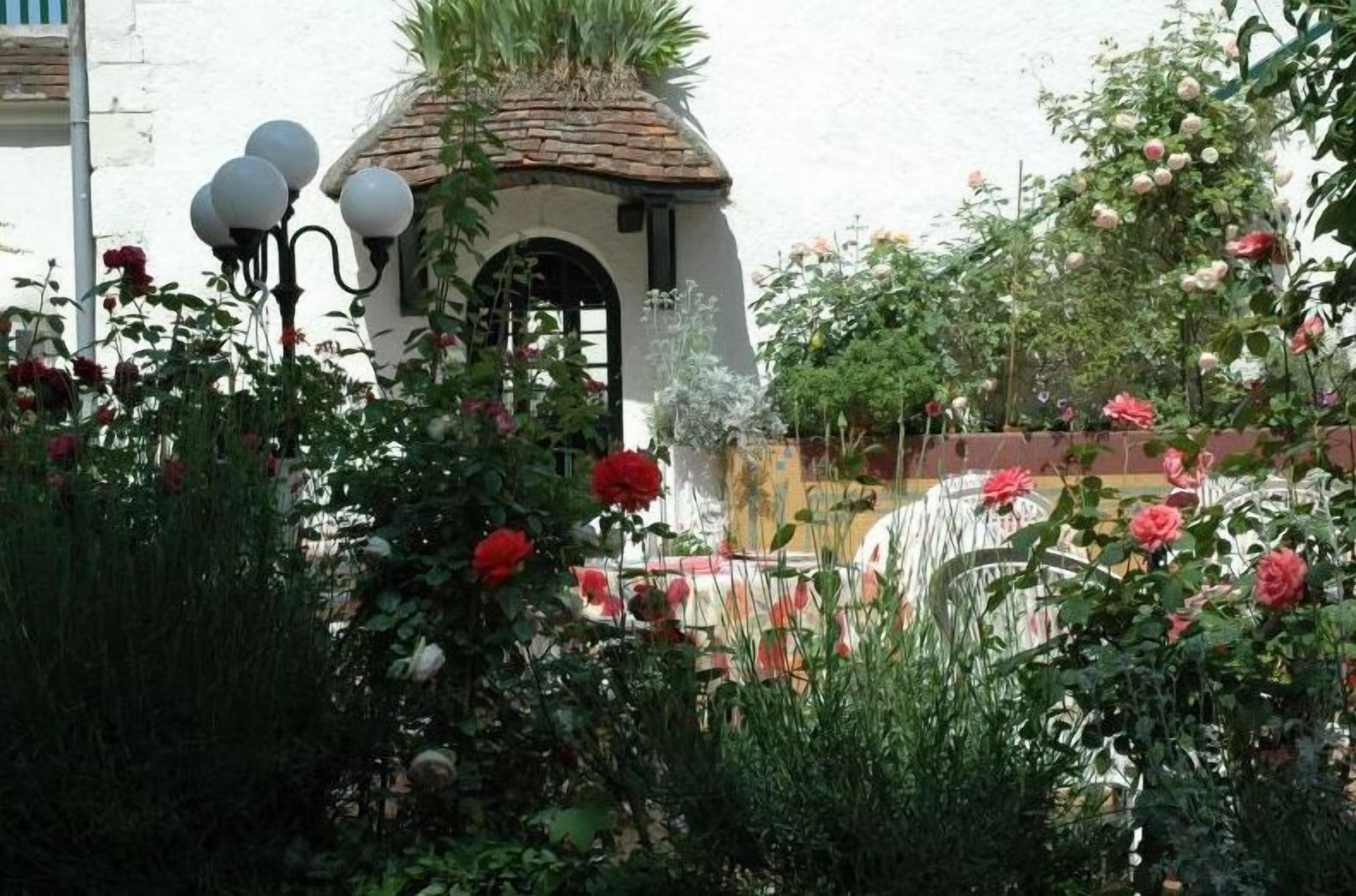A garden with a white building featuring a tiled roof and a black arched entrance.