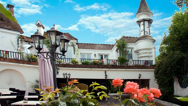 Ein Innenhof mit einem weißen Gebäude, das einen Turm, Sitzgelegenheiten im Freien und Blumenarrangements zeigt.