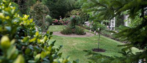 A well-maintained garden with a variety of trees and shrubs, a central flower bed, and a lawn.