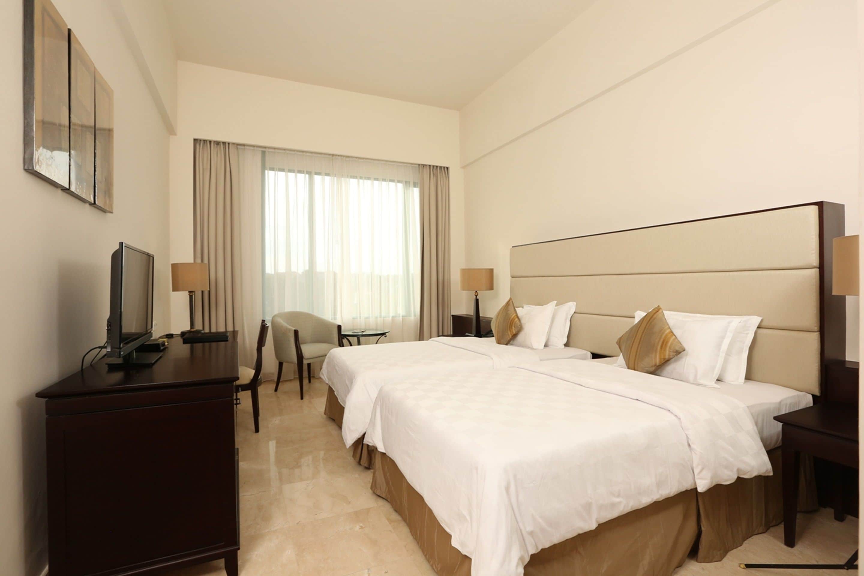 A hotel room with a large bed, a desk, a chair, and a television.