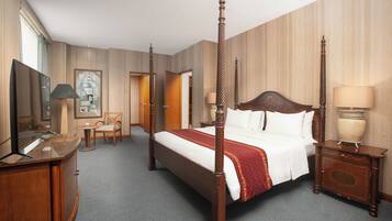 A four-poster bed with a red and white bedspread, a wooden nightstand with a lamp, a desk with a mirror, and a chair.