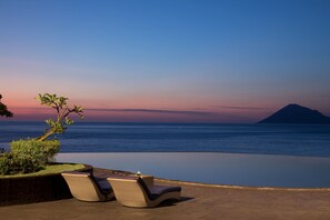 An infinity pool with lounge chairs, a view of the ocean, and a mountain in the distance. - Aryaduta Manado (Manado)
