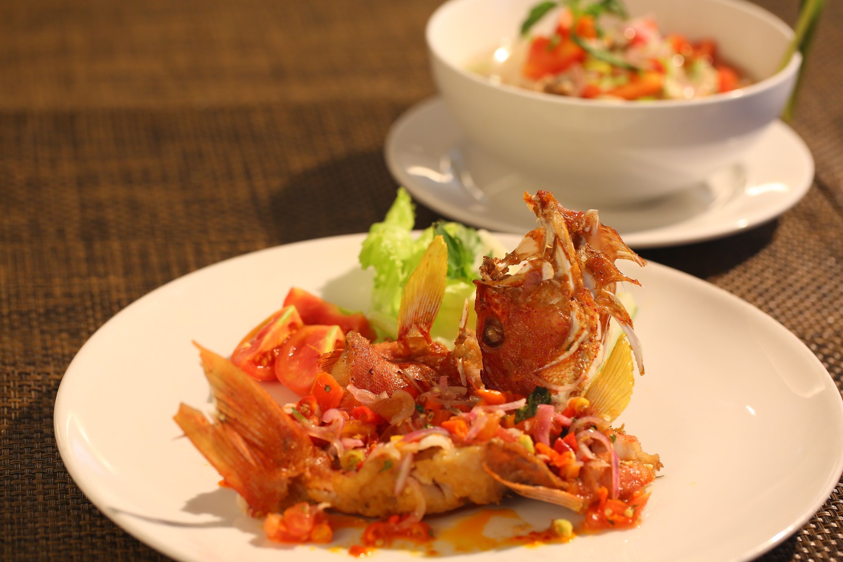 A plate with a fish dish and a bowl of salad in the background.