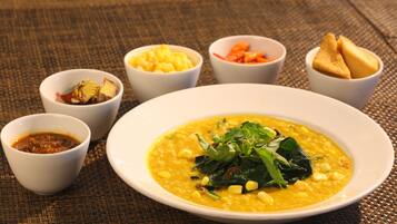 A bowl of lentil soup with corn and greens, accompanied by small bowls of condiments and bread.