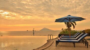 A poolside area with lounge chairs and an umbrella, overlooking a body of water and a distant mountain.