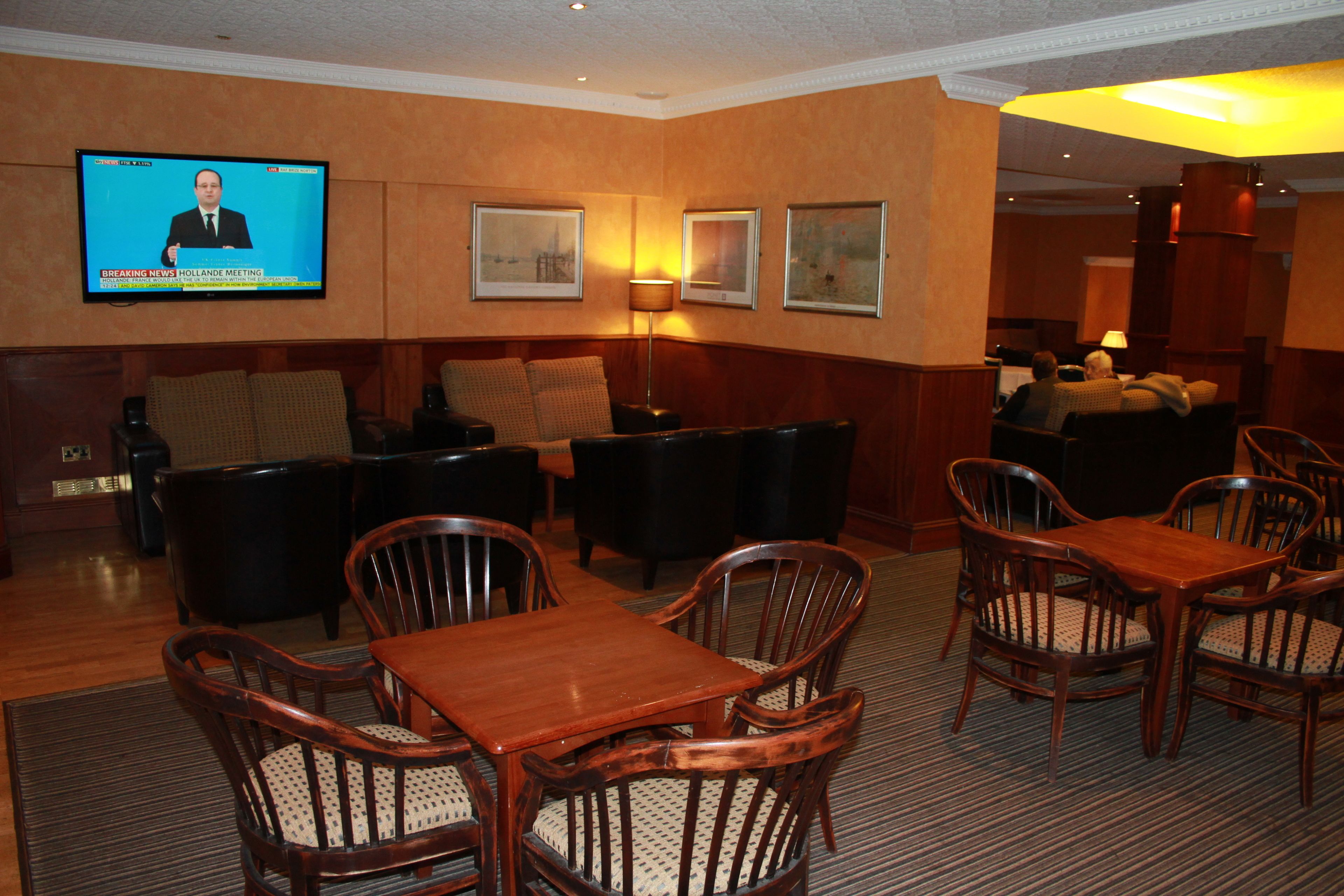 A hotel lobby with a television displaying news, a seating area with sofas and chairs, and framed artwork on the walls.