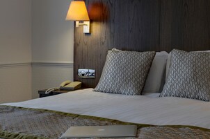 Una habitación de hotel con una cama, una lámpara de noche, un teléfono y un ordenador portátil sobre la cama.
