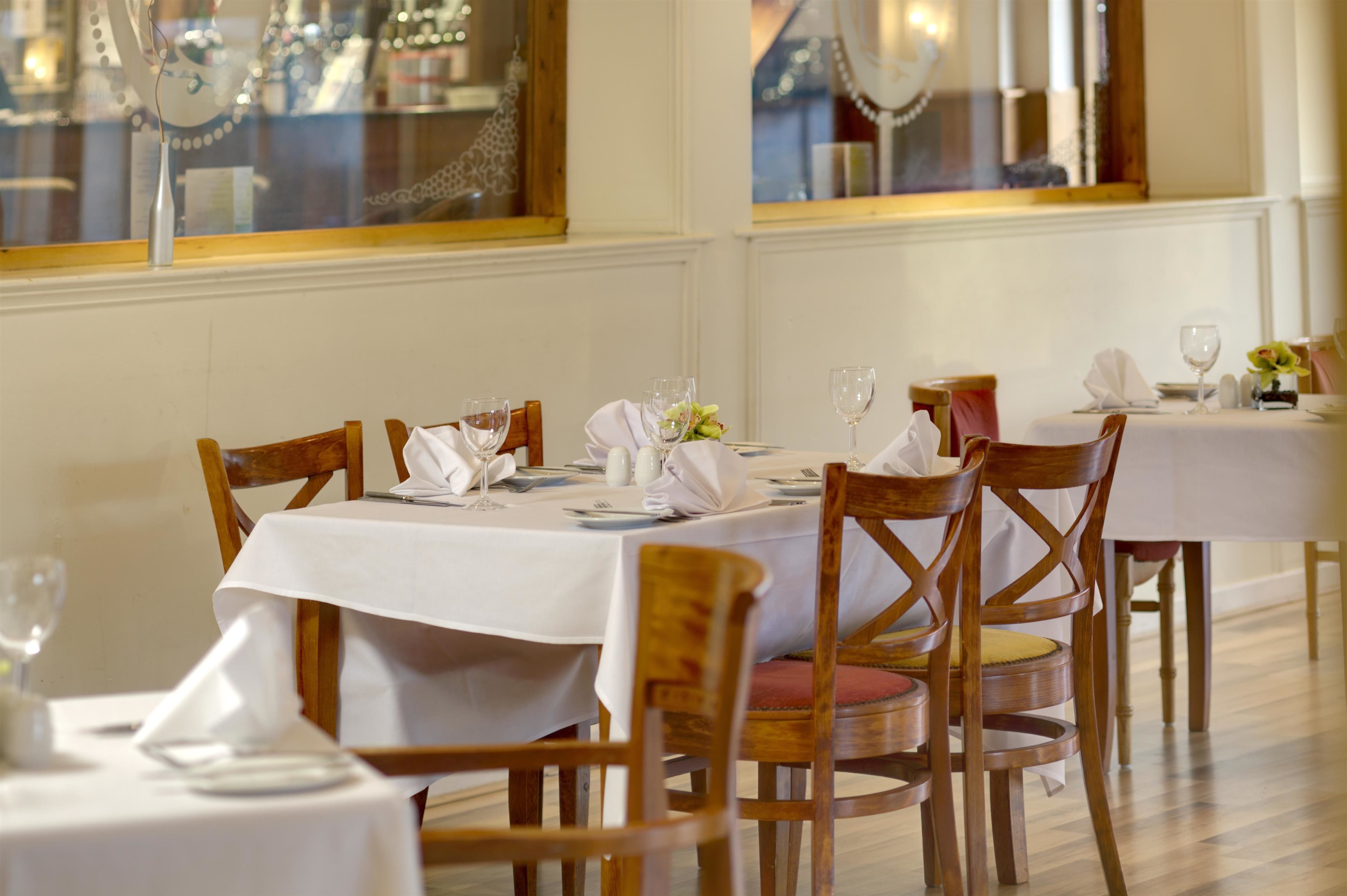 Un espace repas avec des tables dressées pour le repas, des chaises en bois et une nappe blanche.