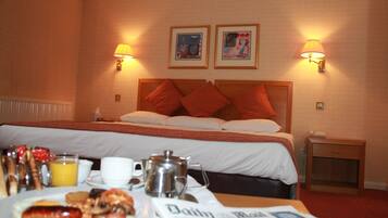 Una camera d'albergo con un letto, abat-jour, un comodino, un tavolo con prodotti per la colazione e due quadri appesi al muro.