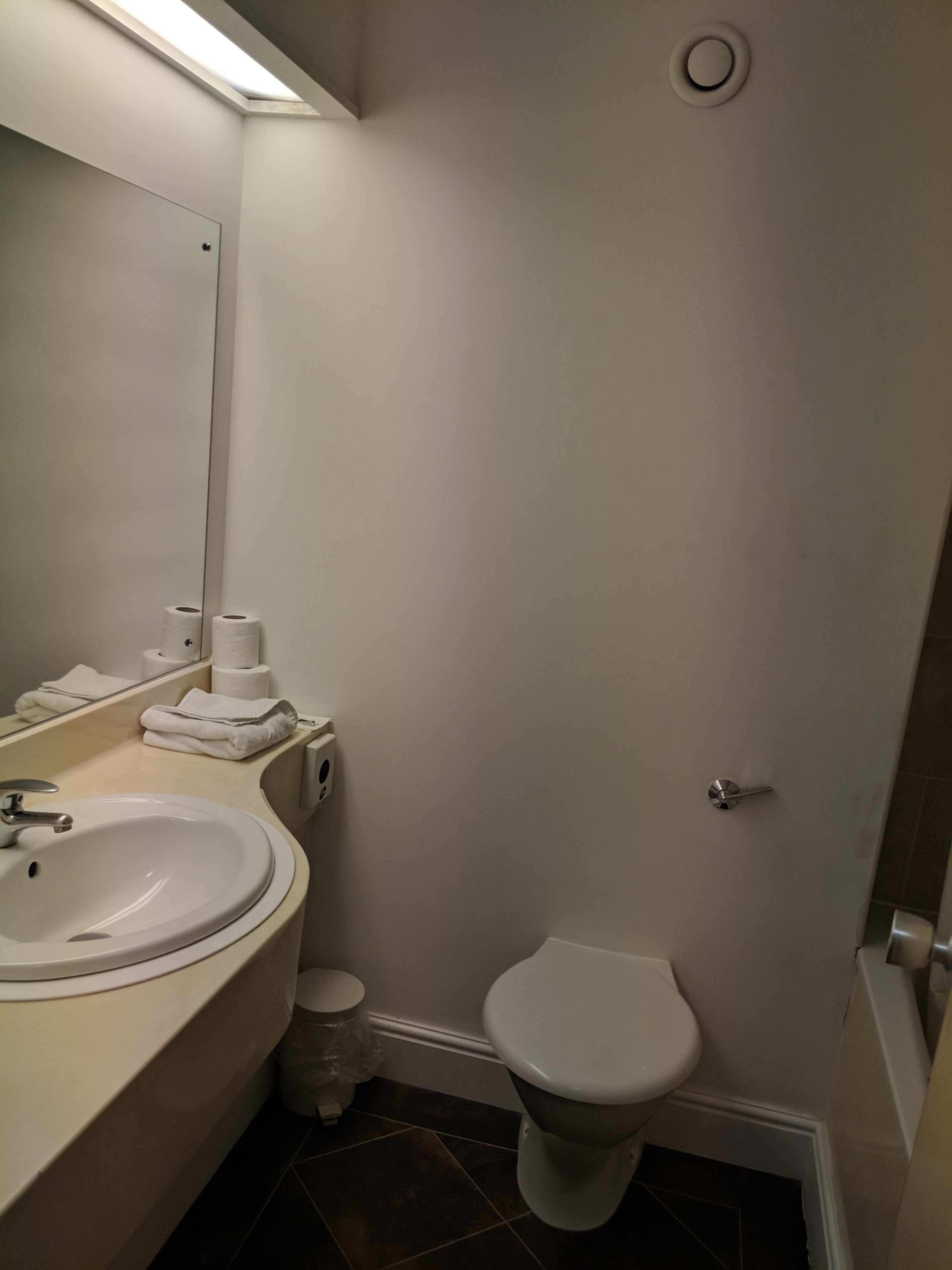 Un baño con lavamanos, espejo, inodoro y dispensador de toallas.