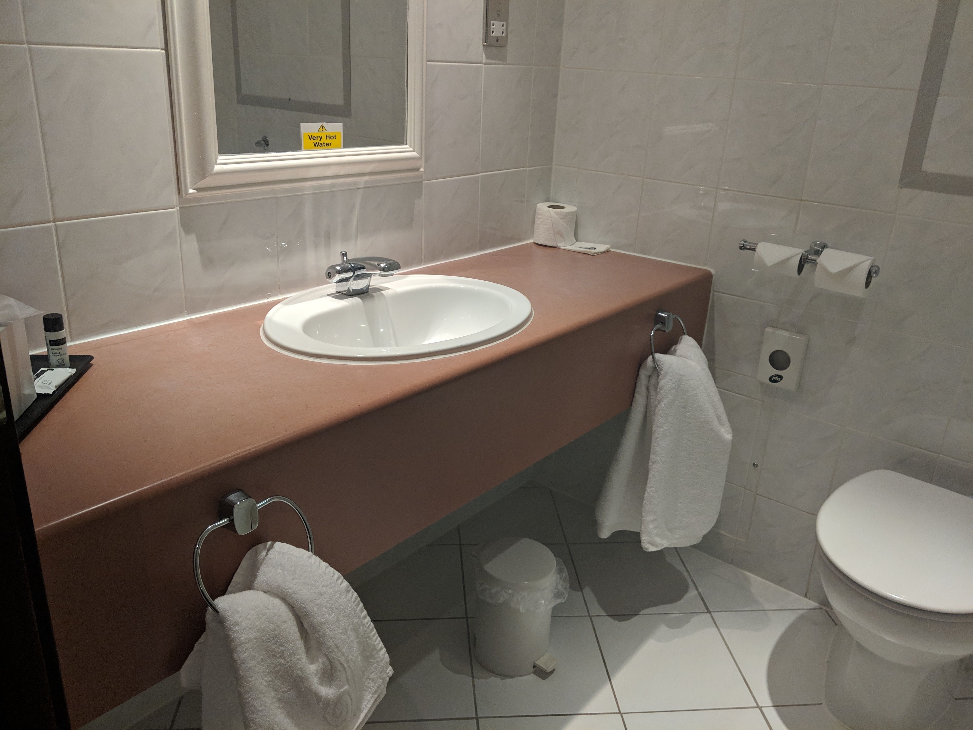 A bathroom with a white sink, a mirror, a toilet, and a trash bin.