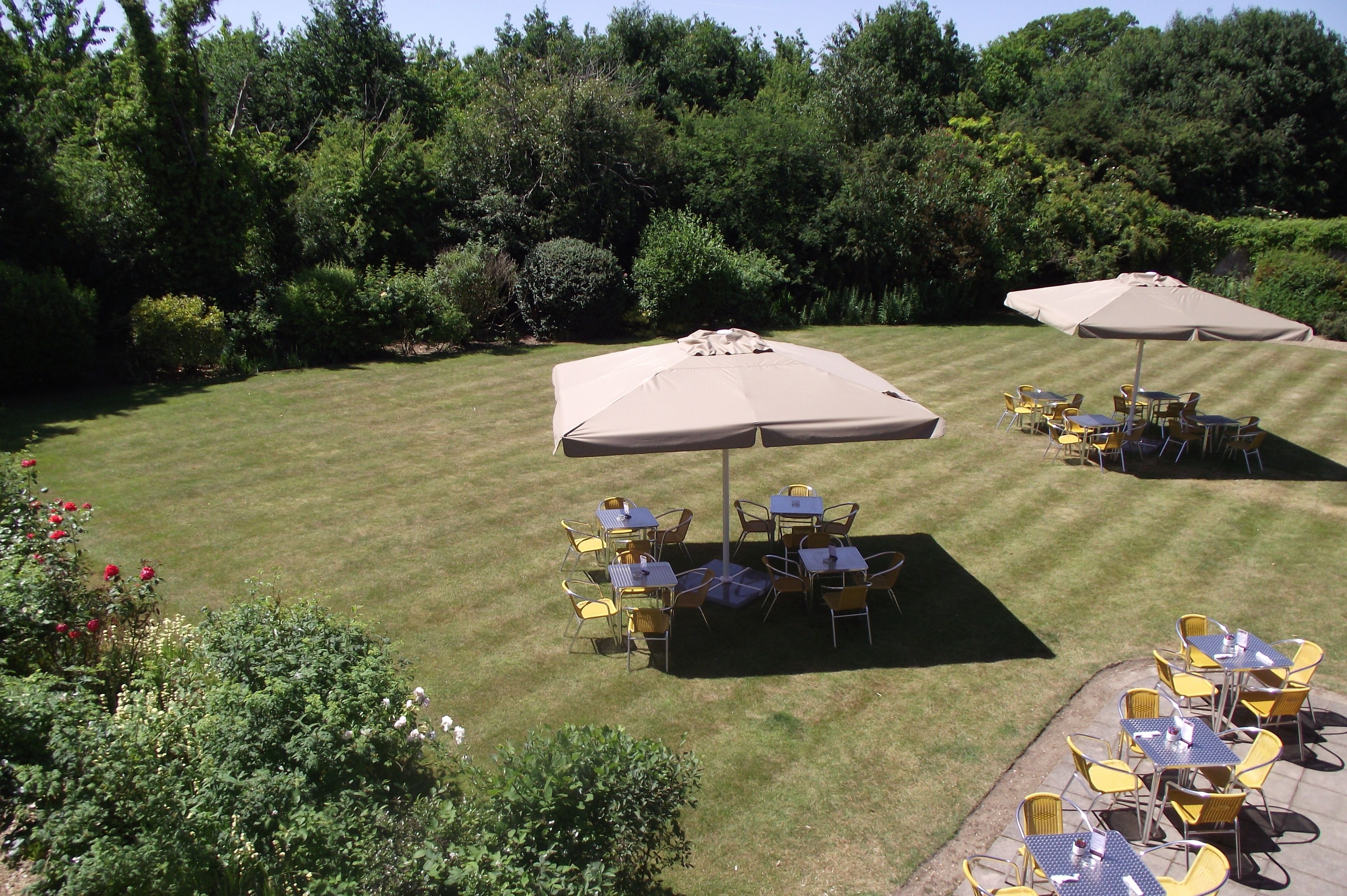 An outdoor patio with tables and chairs under umbrellas, surrounded by greenery.