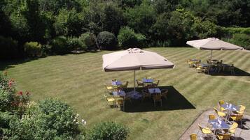 An outdoor patio with tables and chairs under umbrellas, surrounded by greenery.