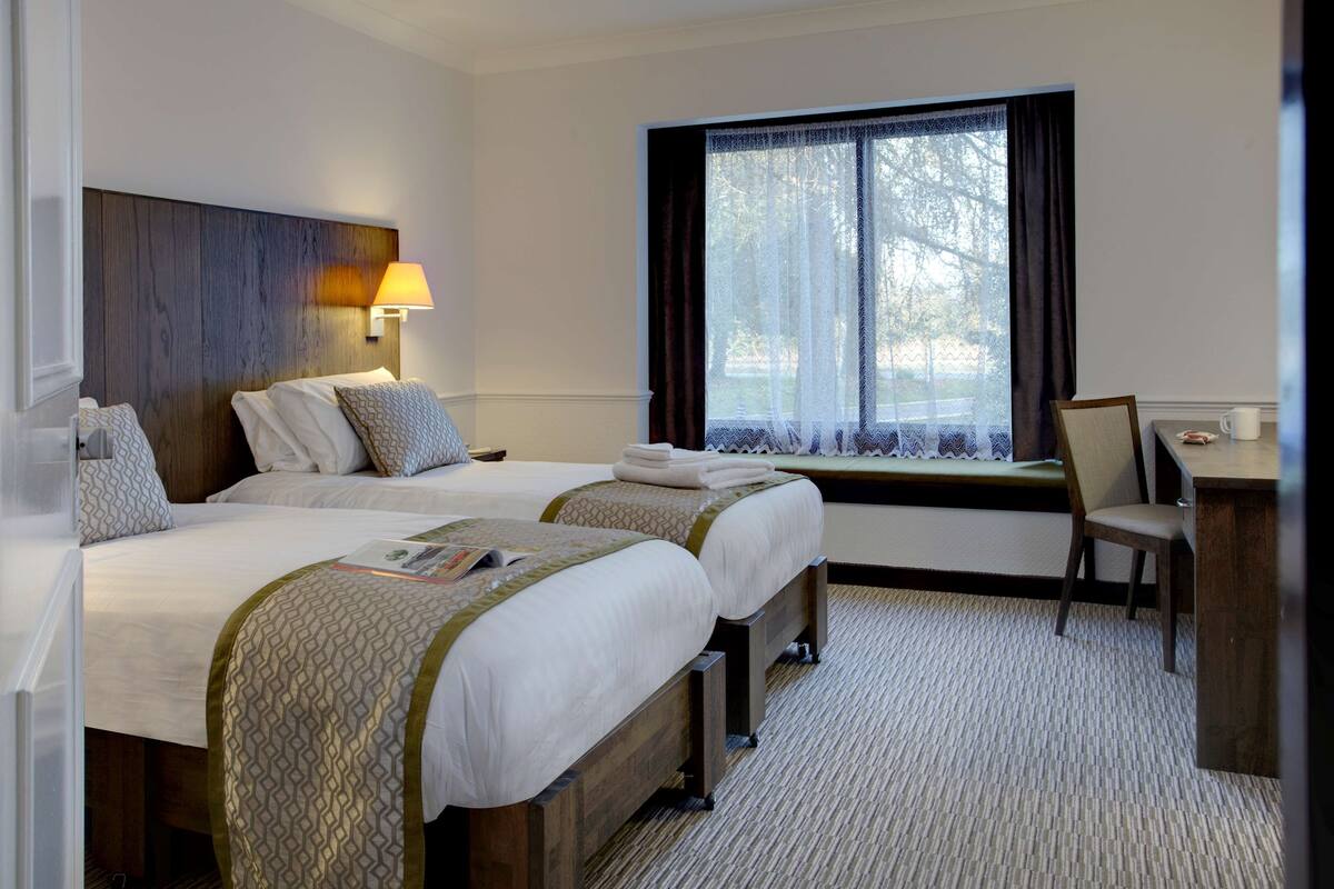 A hotel room with two beds, a desk, a chair, and a window with curtains.