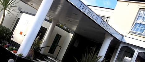 The exterior of the Ipswich Hotel with a covered entrance, white columns, and a reception area.