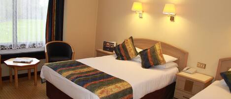 A hotel room with two beds, a desk, and a chair. There are two bedside lamps and a window with curtains.