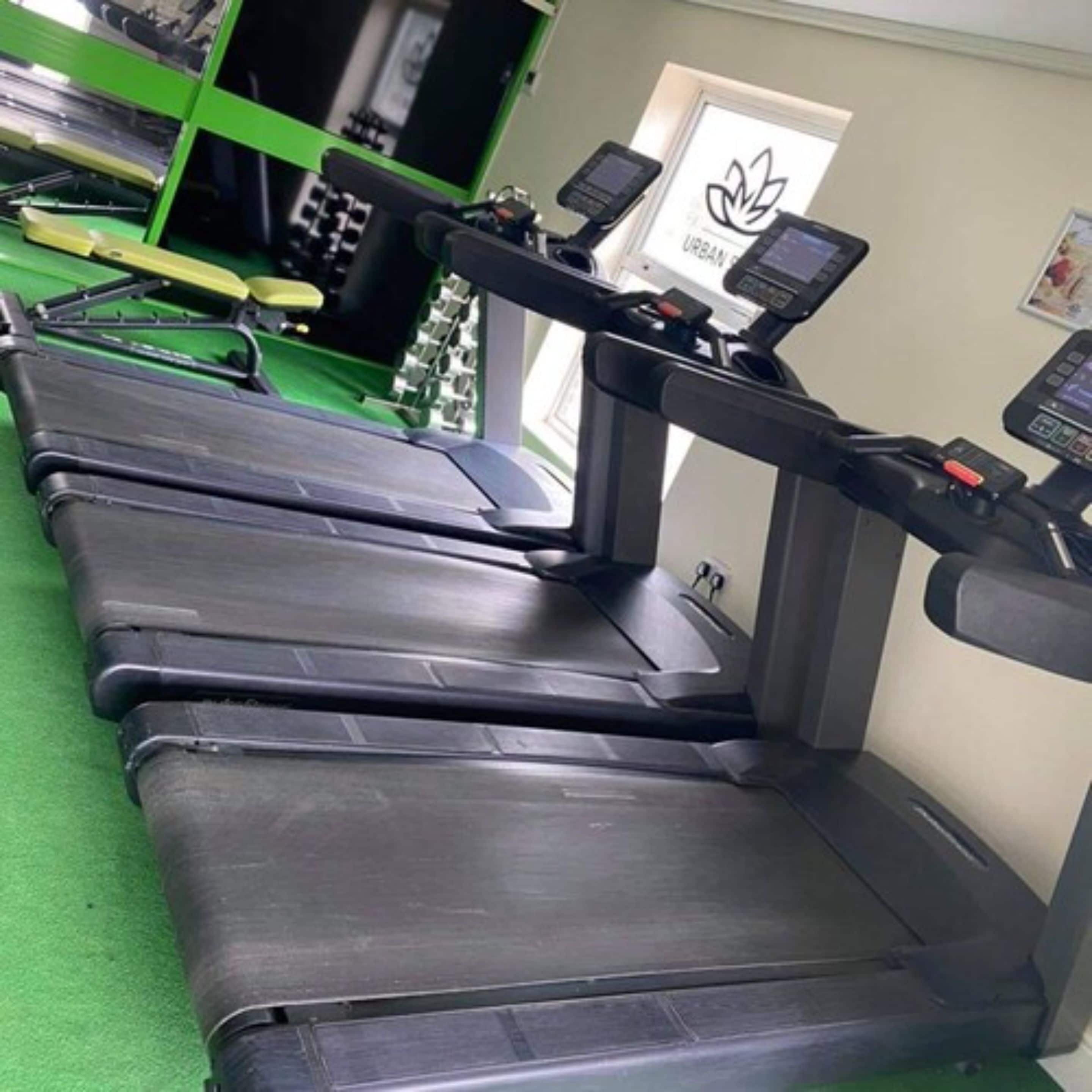 Varias cintas de correr en un gimnasio con suelo verde y un letrero con un logo de flor de loto.