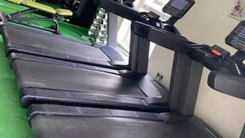 Varias cintas de correr en un gimnasio con suelo verde y un letrero con un logo de flor de loto.