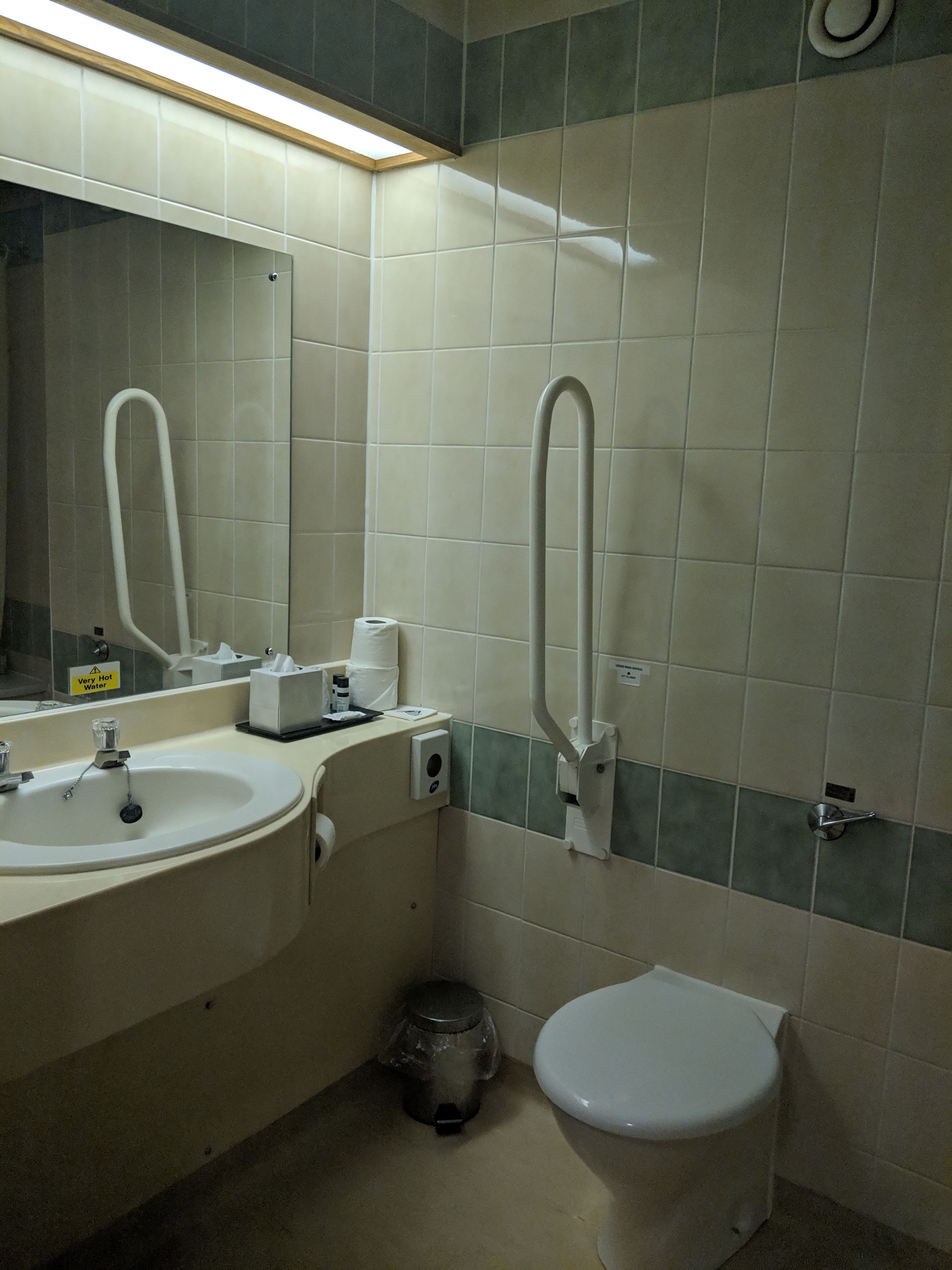 A bathroom with a sink, mirror, toilet, and a trash bin.