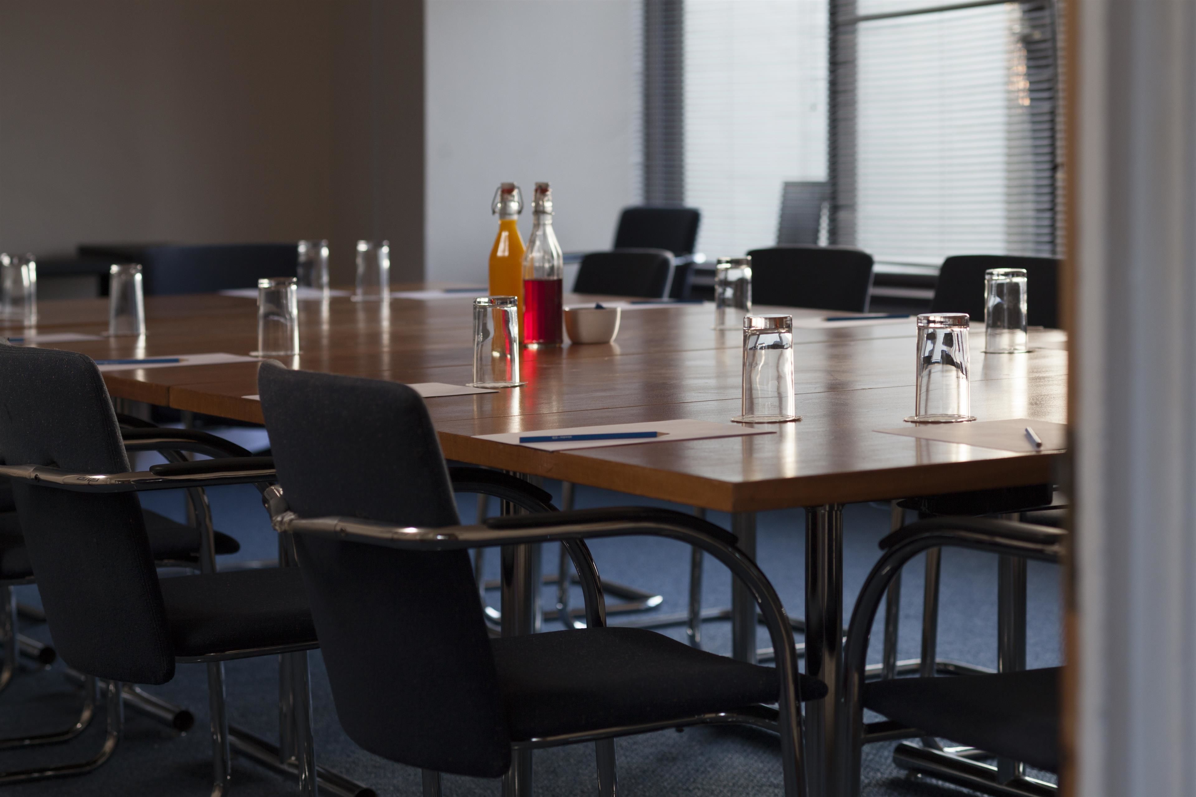 A conference room with a long table, black chairs, and various items like glasses, bottles, and a bowl.