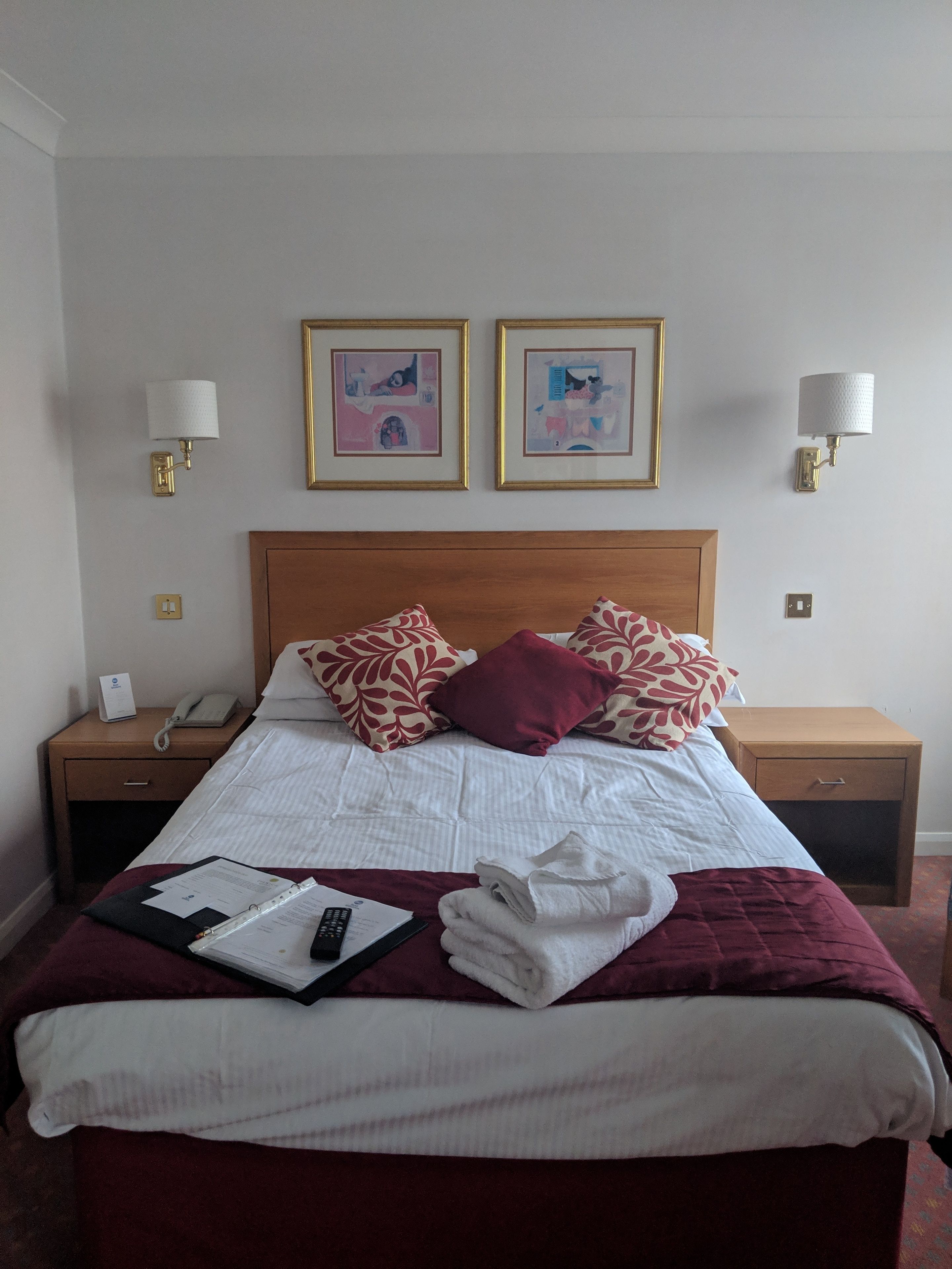 A neatly made bed with a white comforter and red and white patterned pillows, a wooden headboard, and two bedside tables with lamps and a phone.