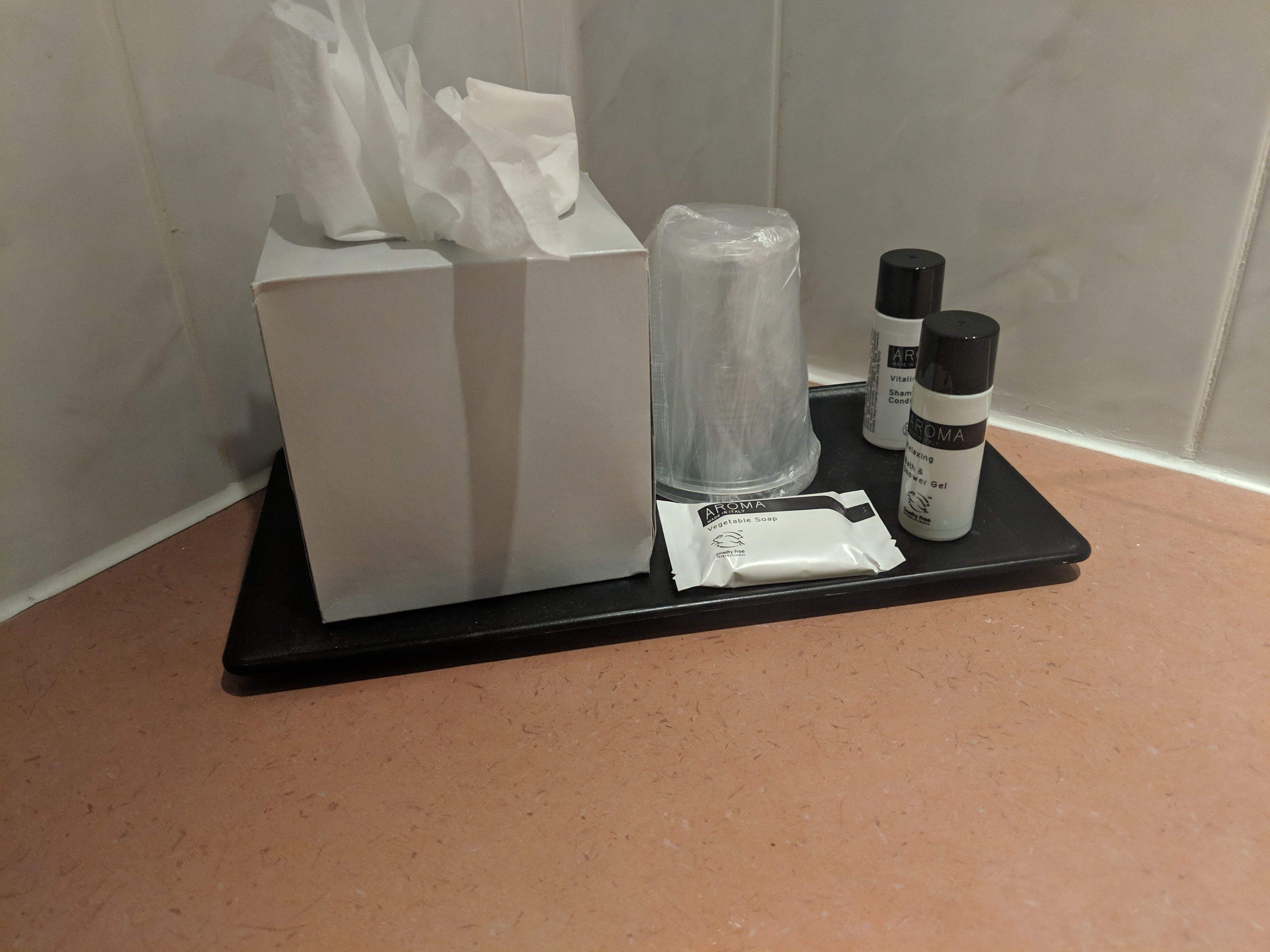A bathroom counter with a tissue box, a clear plastic container, and two bottles of shower gel.
