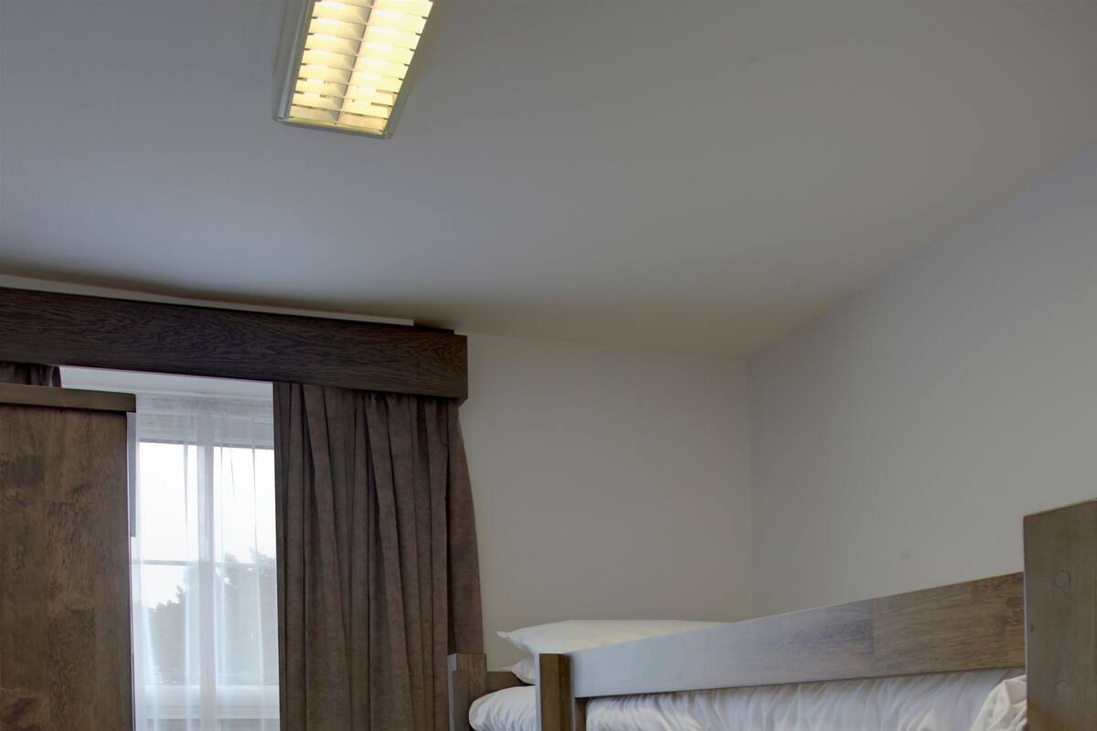 A bunk bed room with a window, curtains, and a radiator.