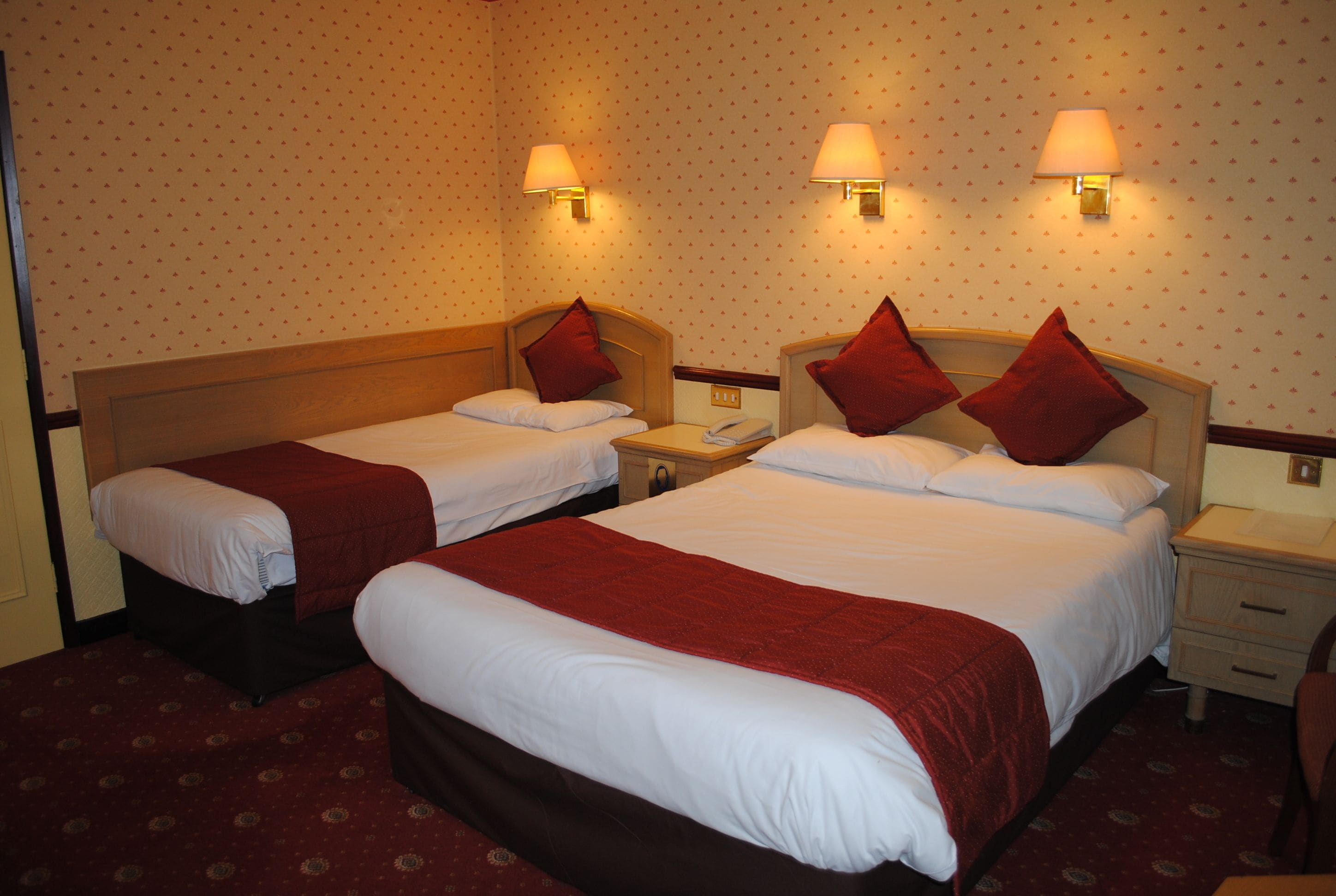 A hotel room with two single beds, each with a red headboard and white bedding. There are two bedside tables with lamps and a telephone. The walls have a polka dot pattern.
