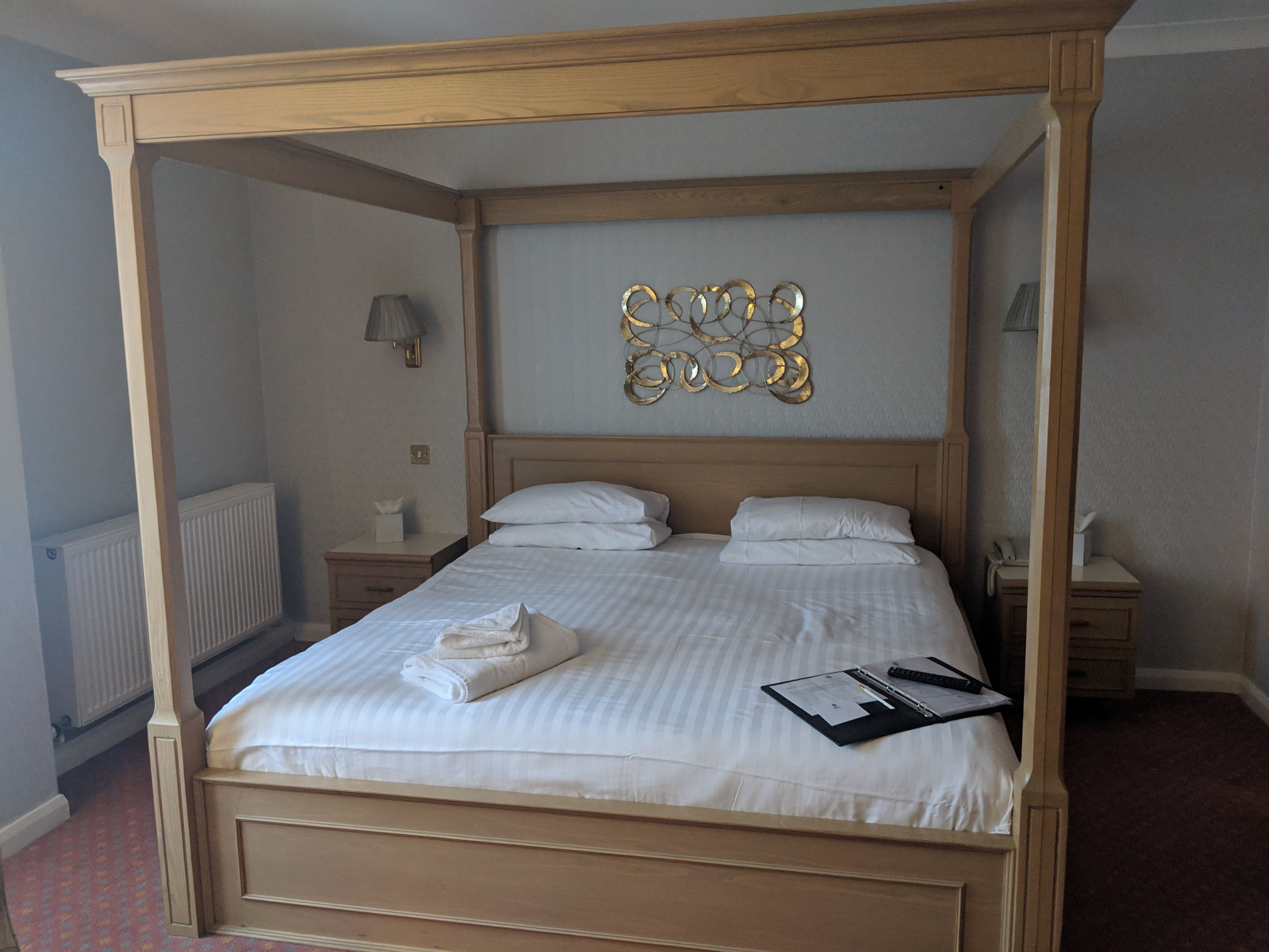 Un lit à baldaquin avec une structure en bois, du linge de lit blanc et un élément décoratif fixé au mur au-dessus.