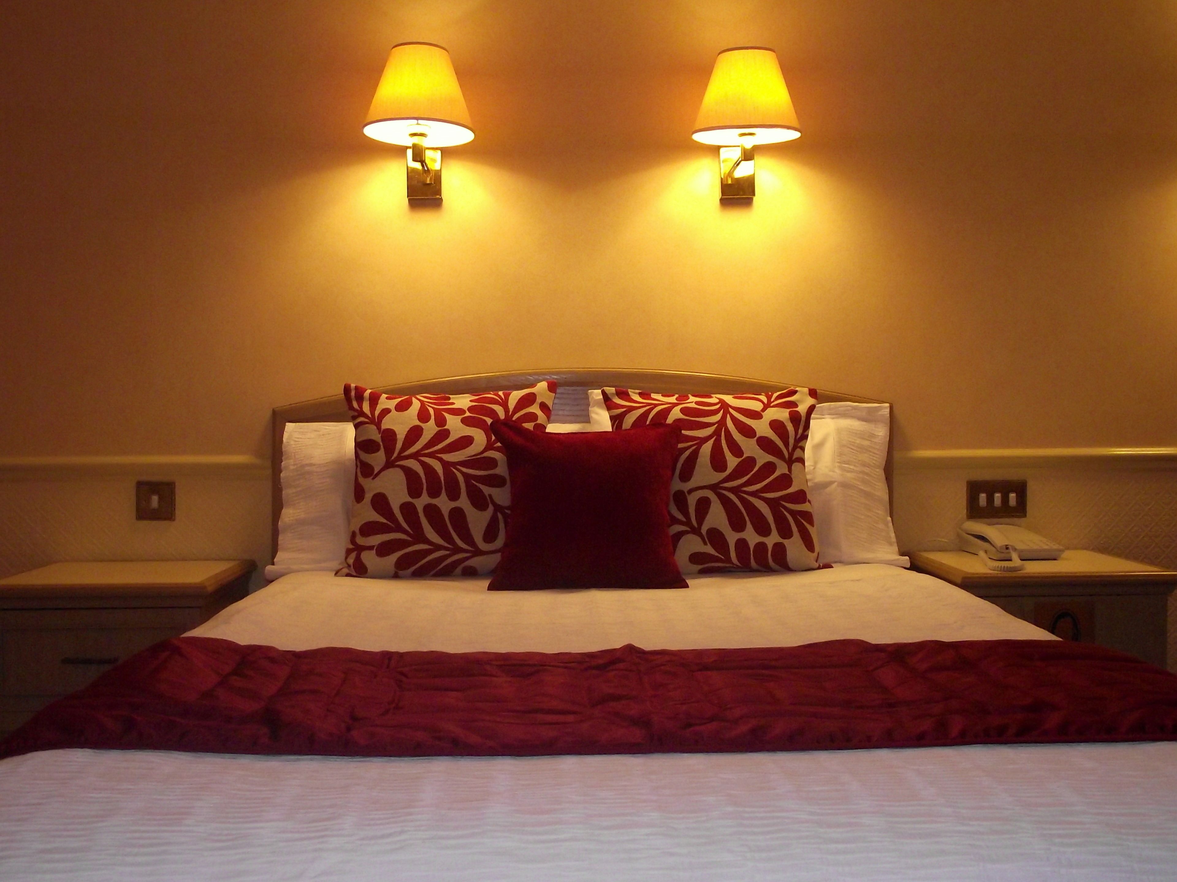 A hotel room with a bed, two bedside lamps, a telephone, and a red throw blanket.