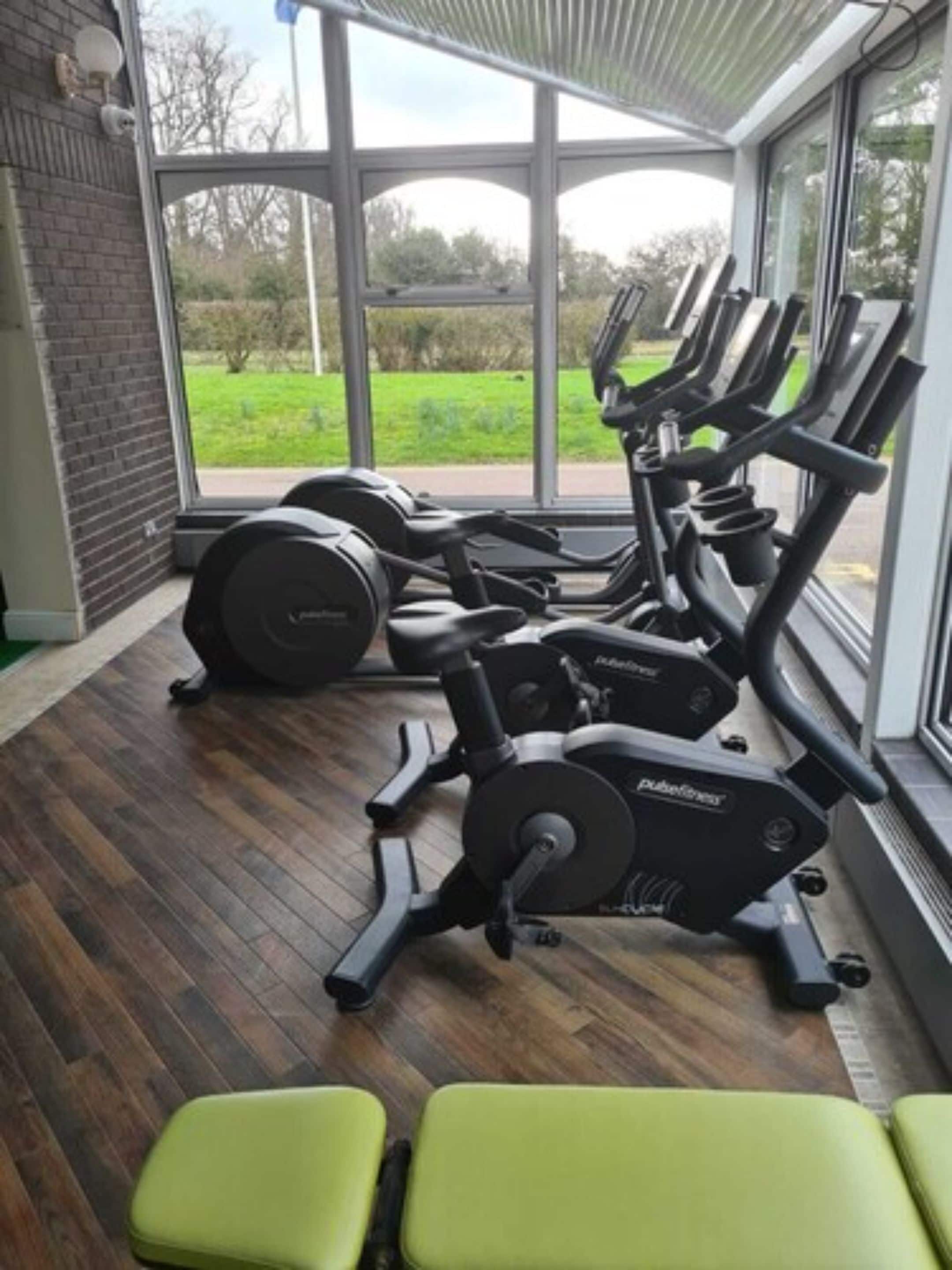 A gym with exercise equipment, a brick wall, and large windows overlooking a green landscape.