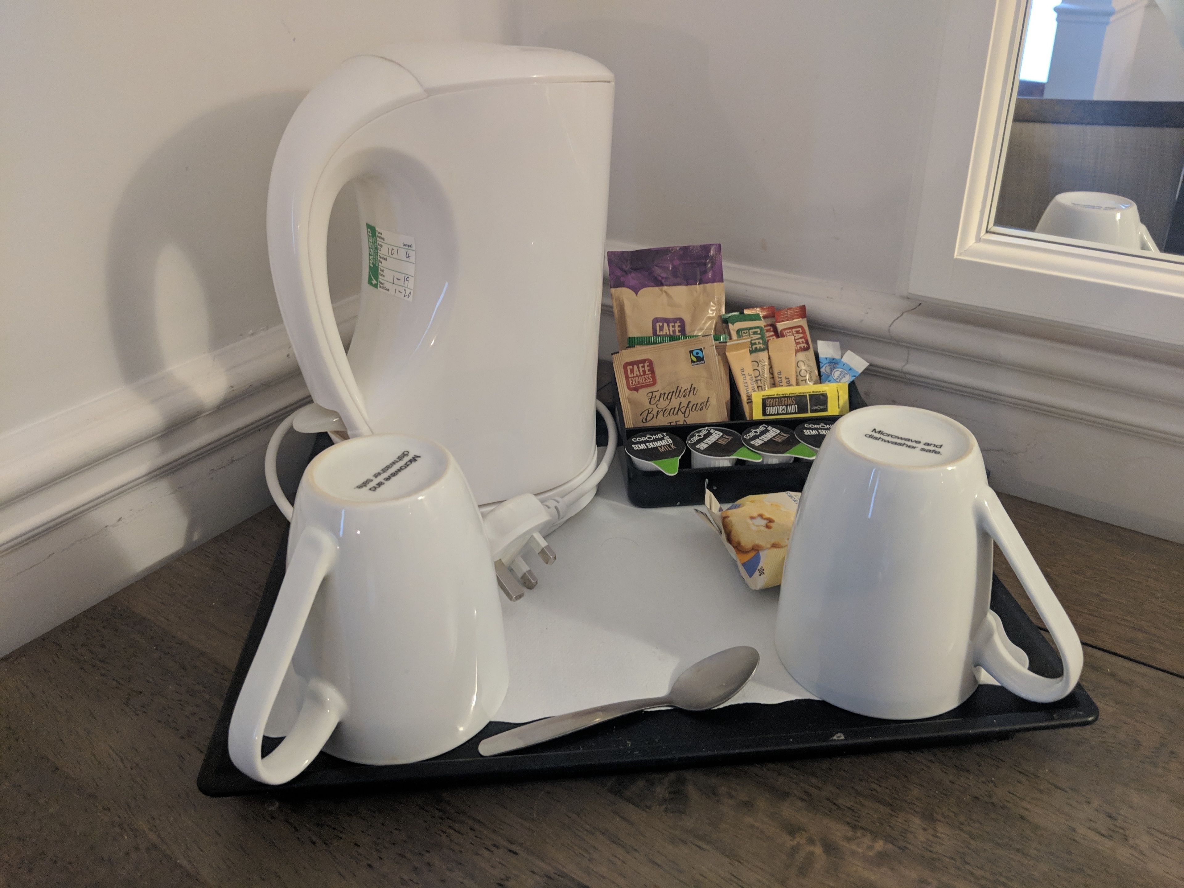 Un plateau de petit-déjeuner avec deux tasses blanches, une machine à café et divers aliments, notamment des boîtes de céréales et un paquet de café.