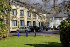 A parking area with several cars, a building with multiple windows, and some greenery. - Best Western Ipswich Hotel (Ipswich)