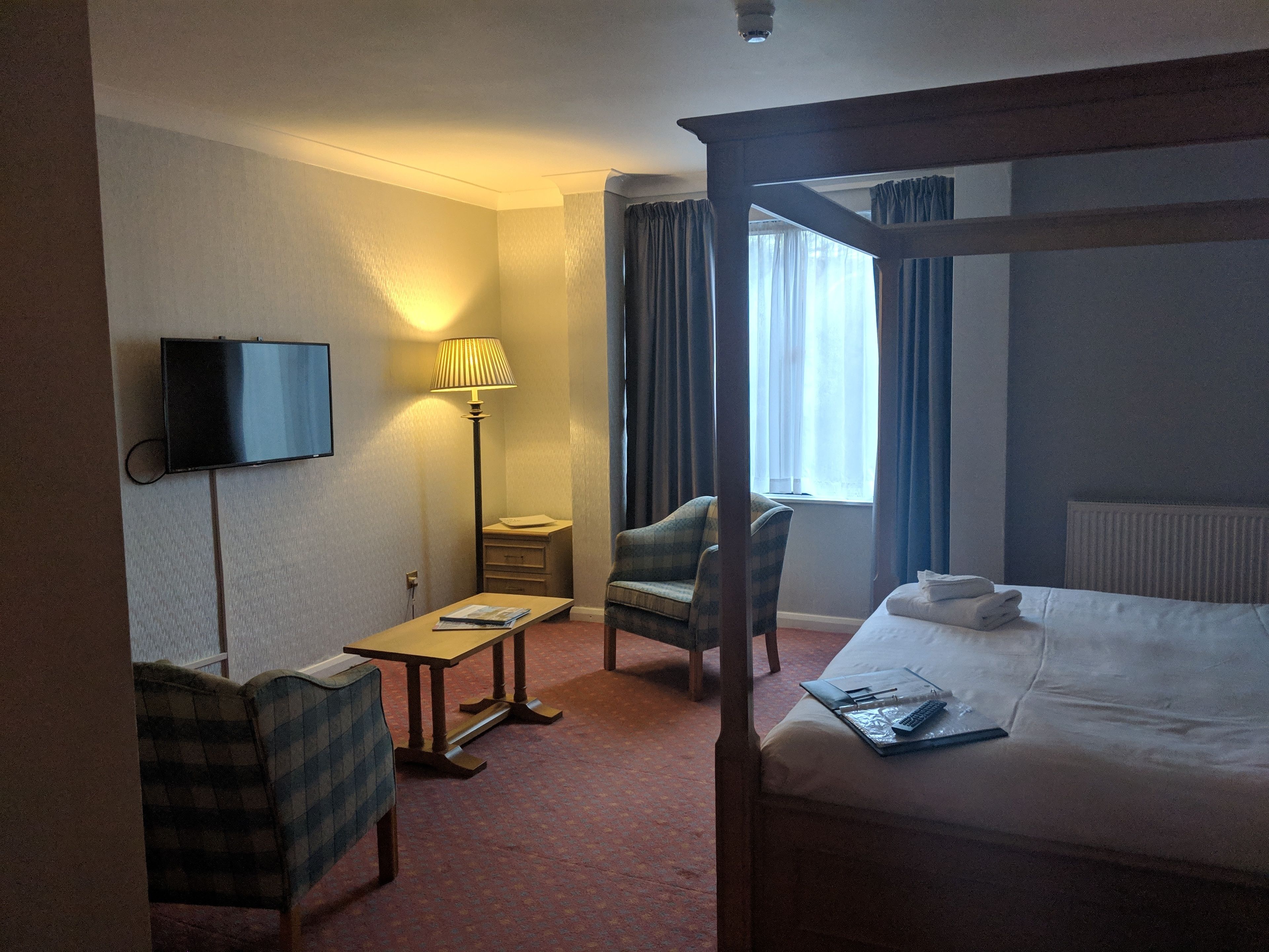 A hotel room with a bed, a desk, a chair, a television, and a lamp.